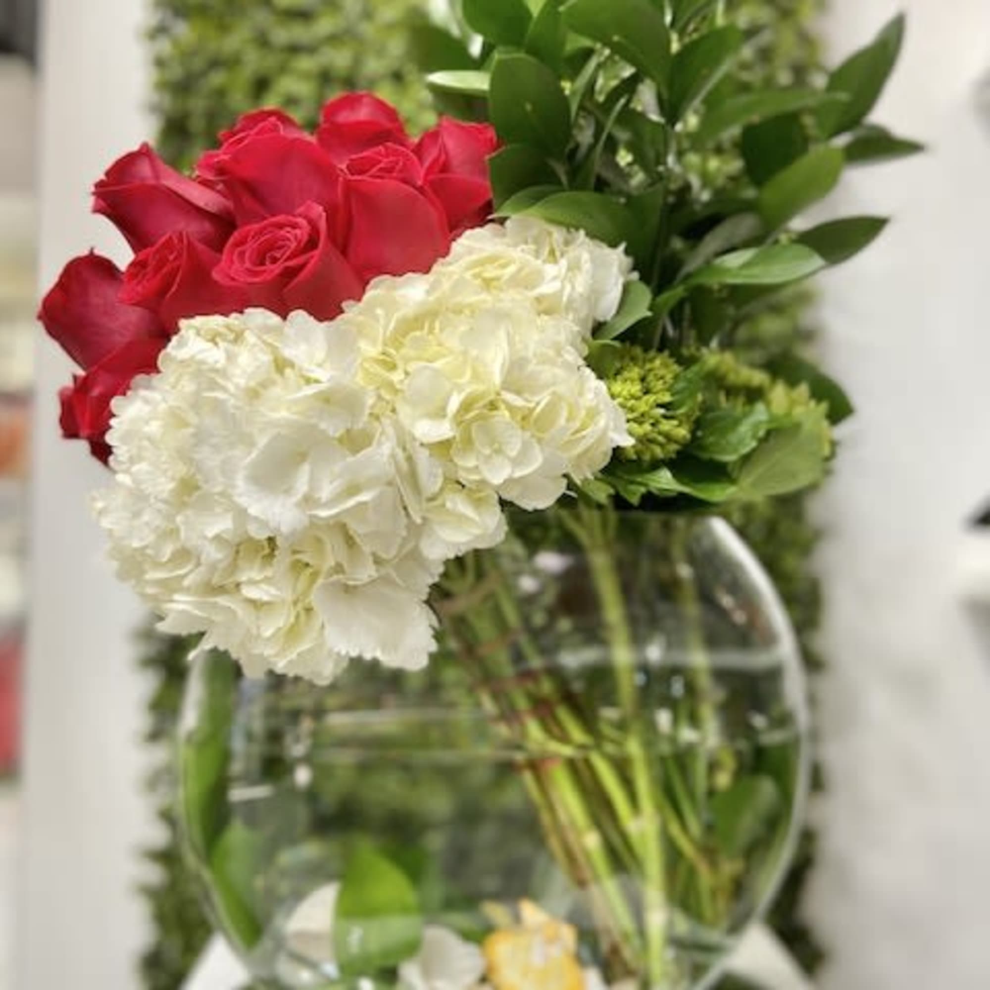 Asymmetrical arrangement of red roses and white hydrangeas in a round clear glass bowl vase