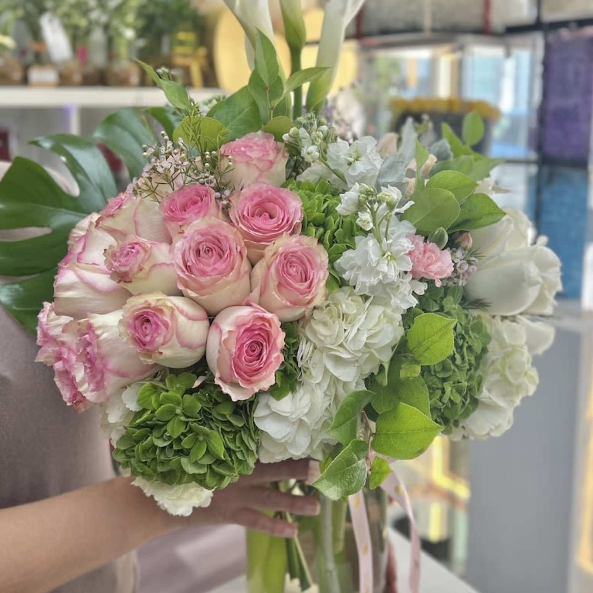 Tall glass vase of pink roses, white hydrangeas, white calla lilies and a large tropical leaf