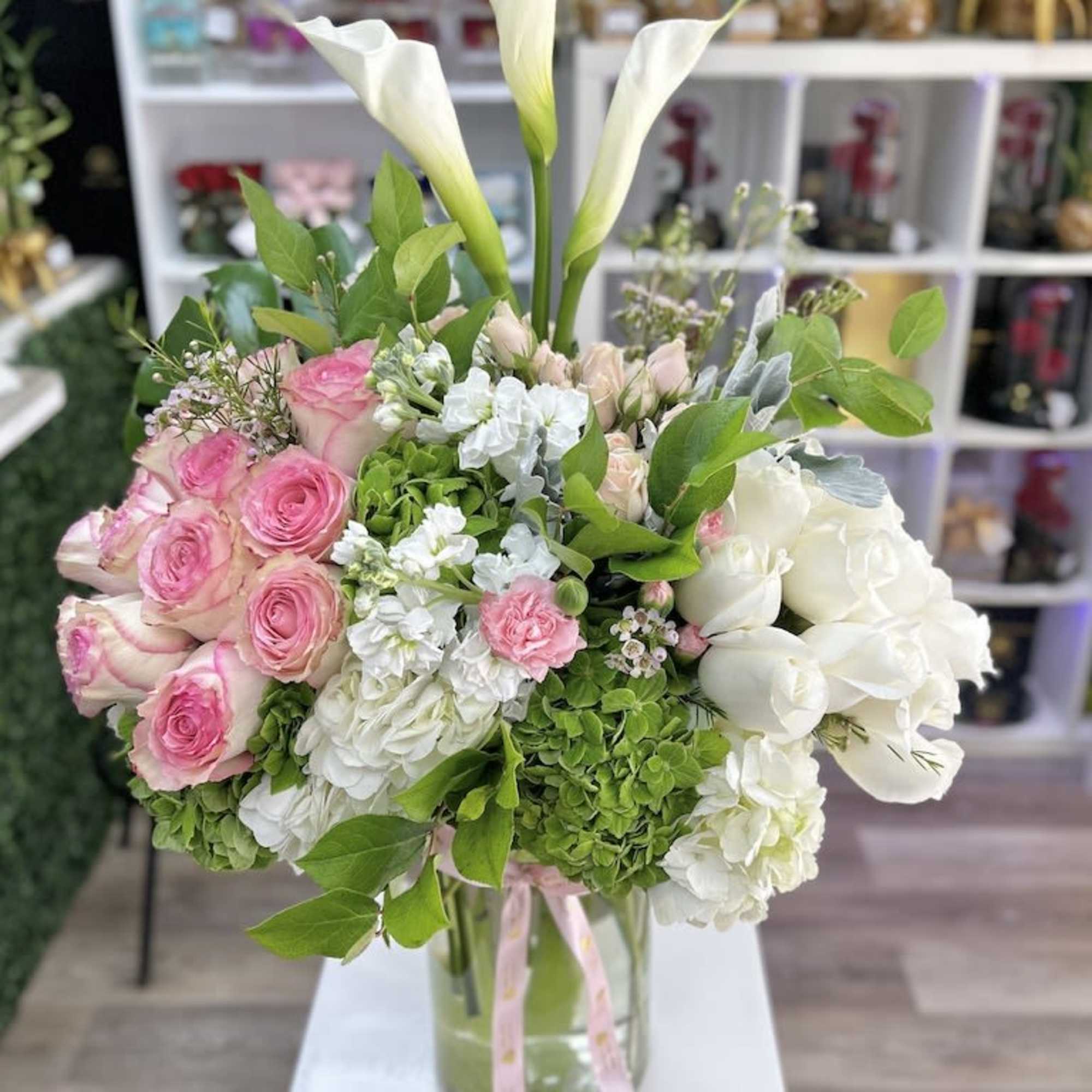 Tall mixed bouquet of white calla lilies, pink roses, and hydrangeas in a clear glass vase