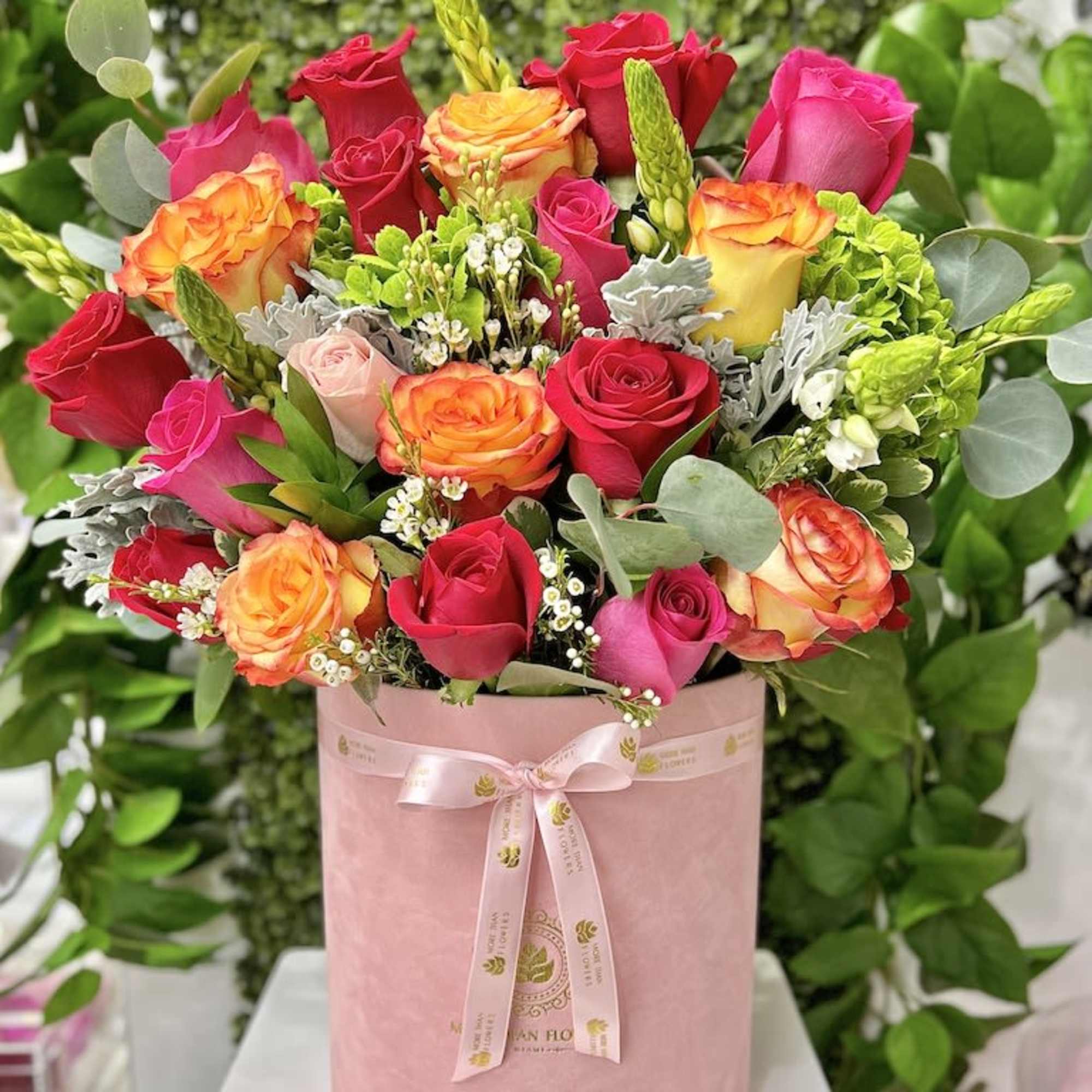 Pink hatbox arrangement of hot pink and orange-yellow roses with white filler flowers