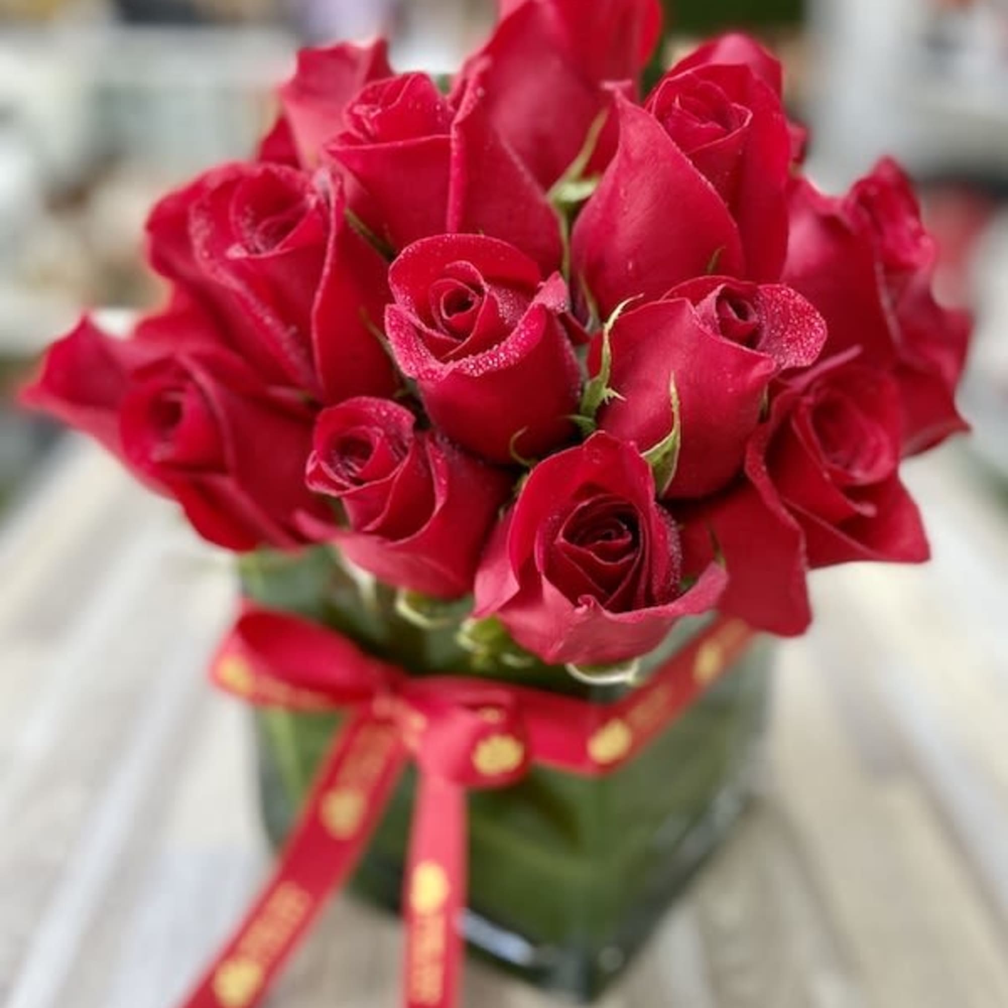 Compact arrangement of red roses in a clear square vase tied with a red ribbon