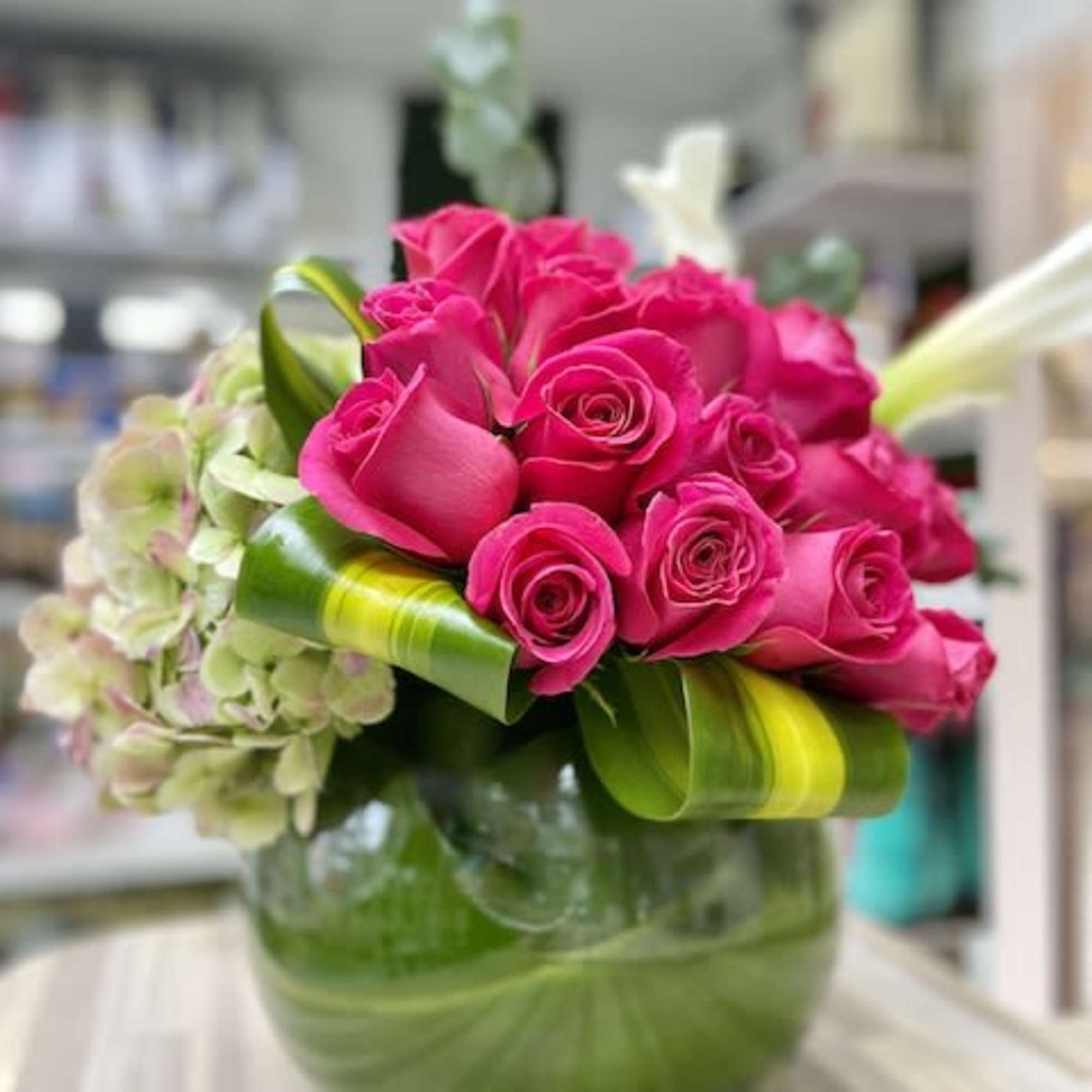 Low glass vase of hot pink roses with pale green hydrangeas and looped green leaves.