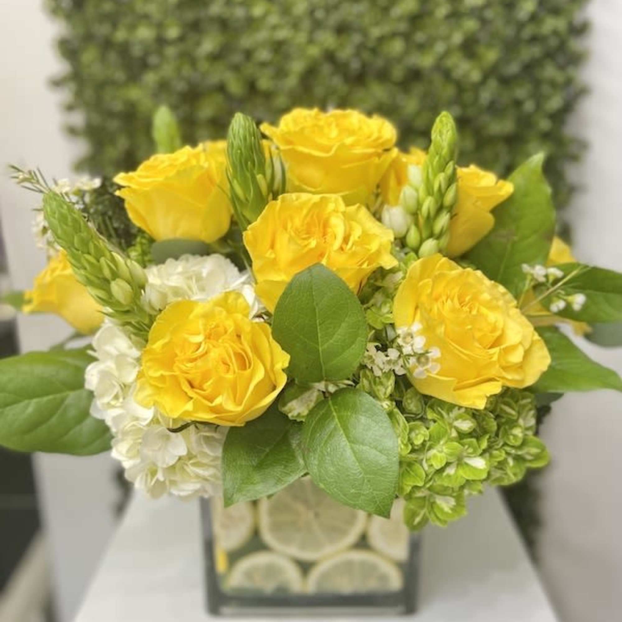 Low arrangement of yellow roses with white flowers in a glass cube vase lined with citrus slices