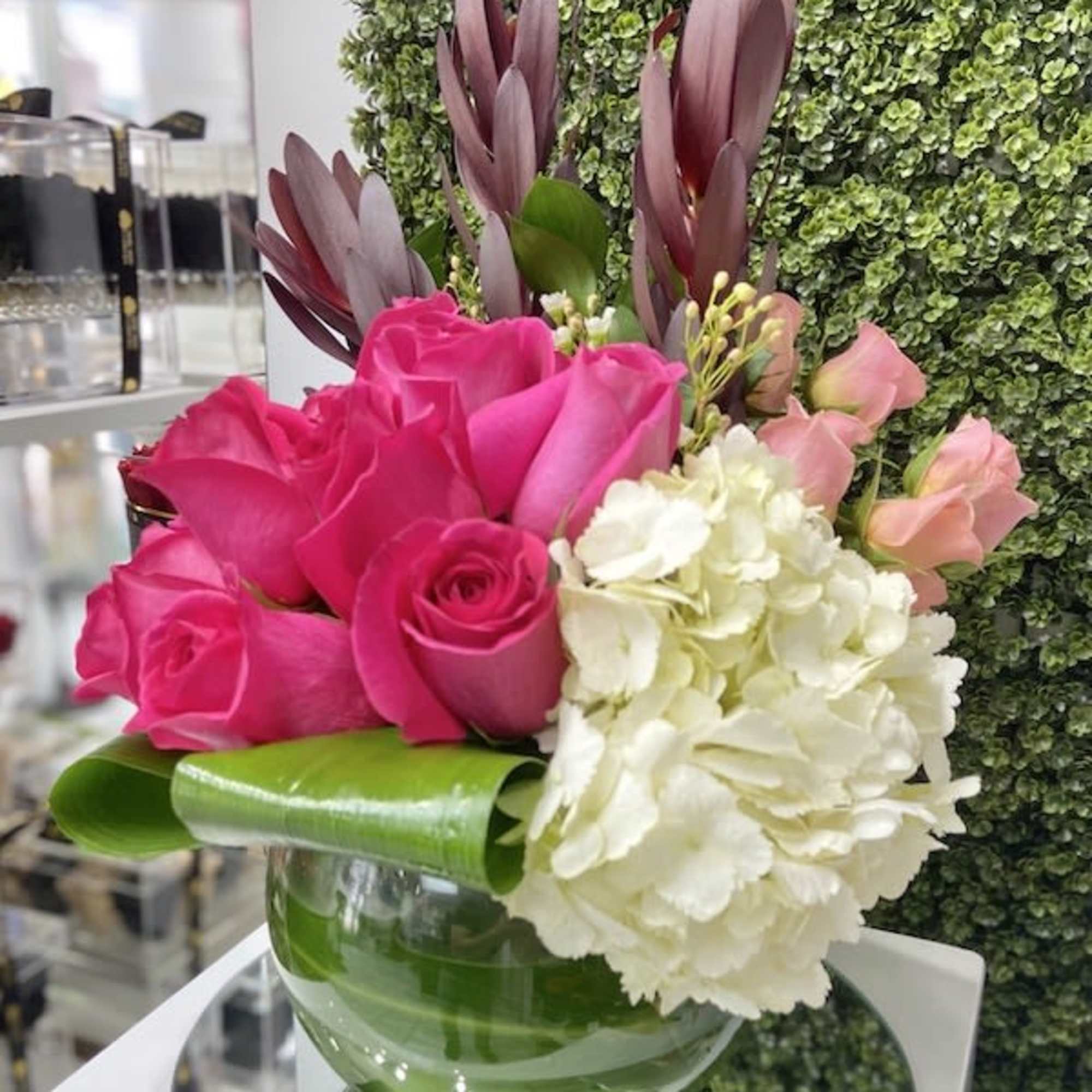Compact arrangement of hot pink roses and white hydrangea in a clear glass bowl vase