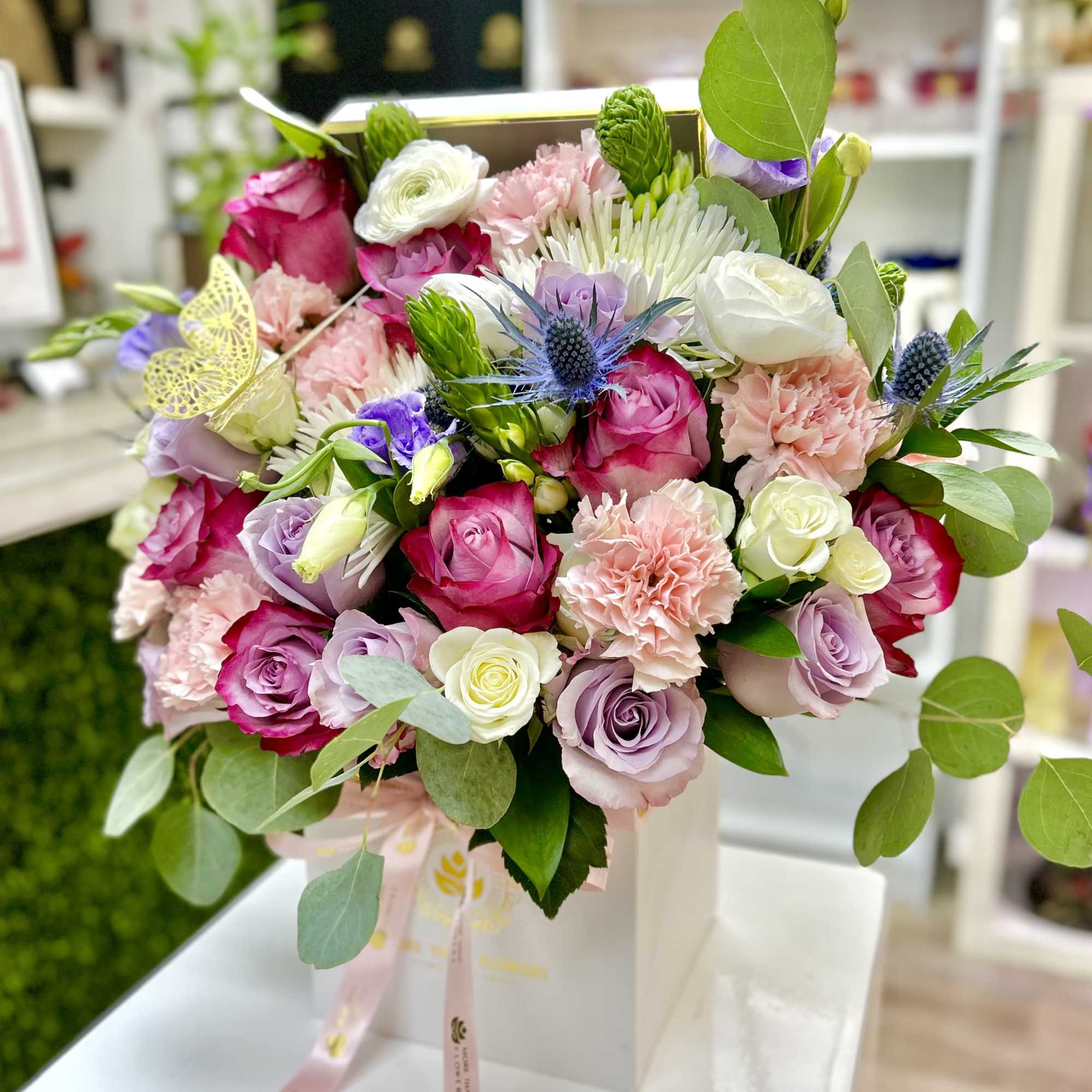 Pink, white, and lavender rose and carnation arrangement in a white box with ribbon and butterfly accent