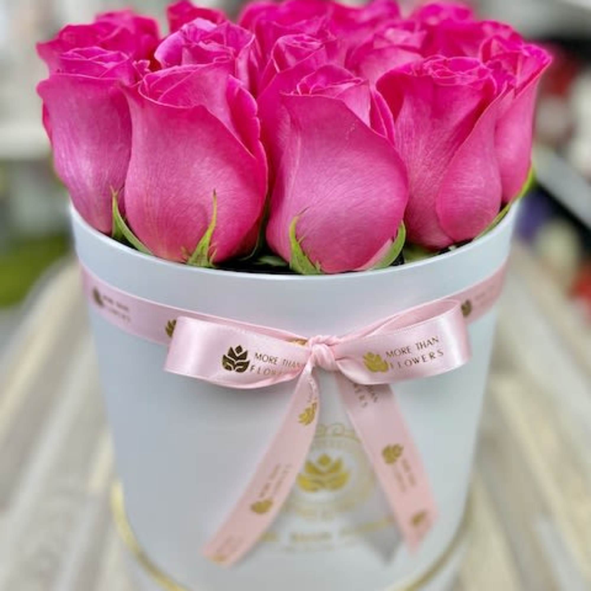 Round box of hot pink roses with a pink ribbon bow around a white hatbox container.