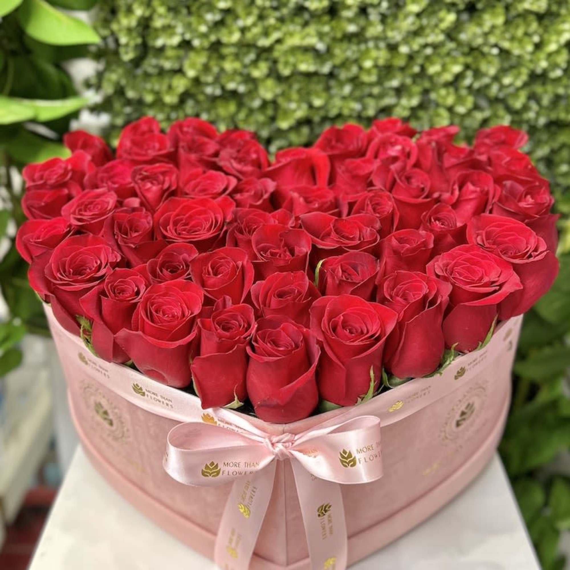 Heart-shaped pink box filled with tightly packed red roses and tied with a satin ribbon