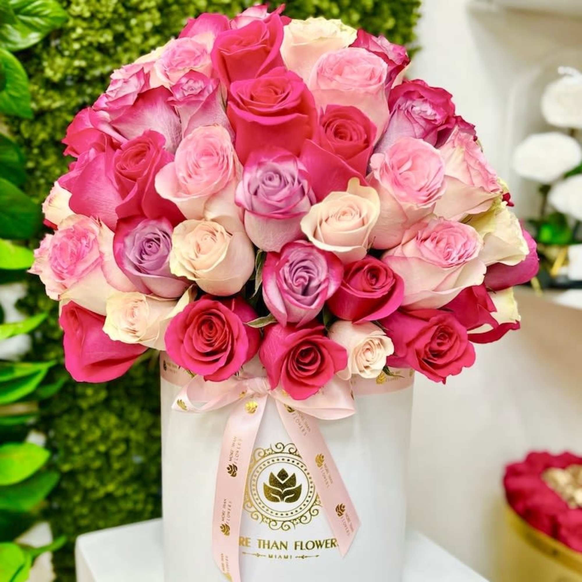 Round hat box arrangement of pink, cream, and lavender roses in a white cylinder box with ribbon.