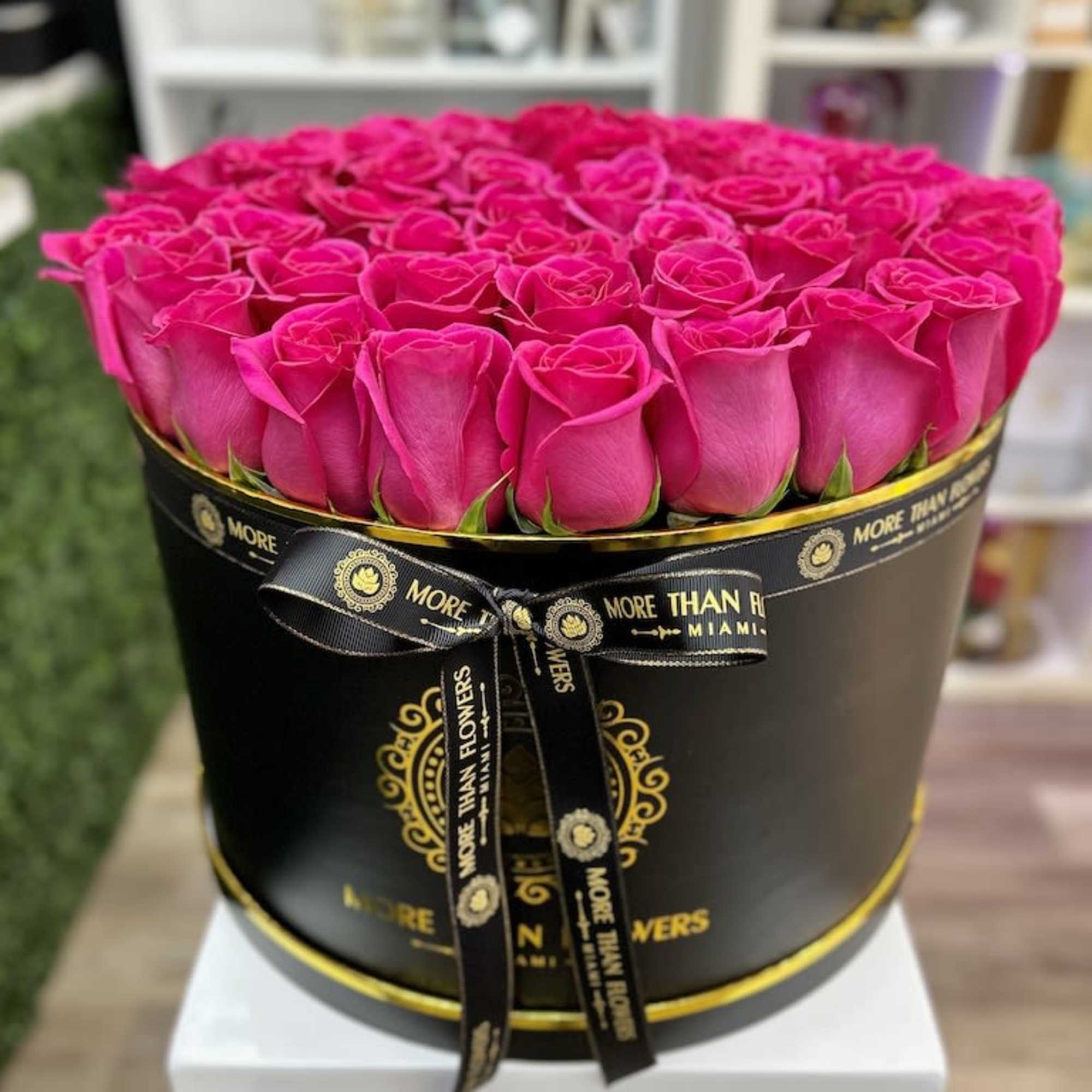 Round black hat box filled with tightly packed hot pink roses.