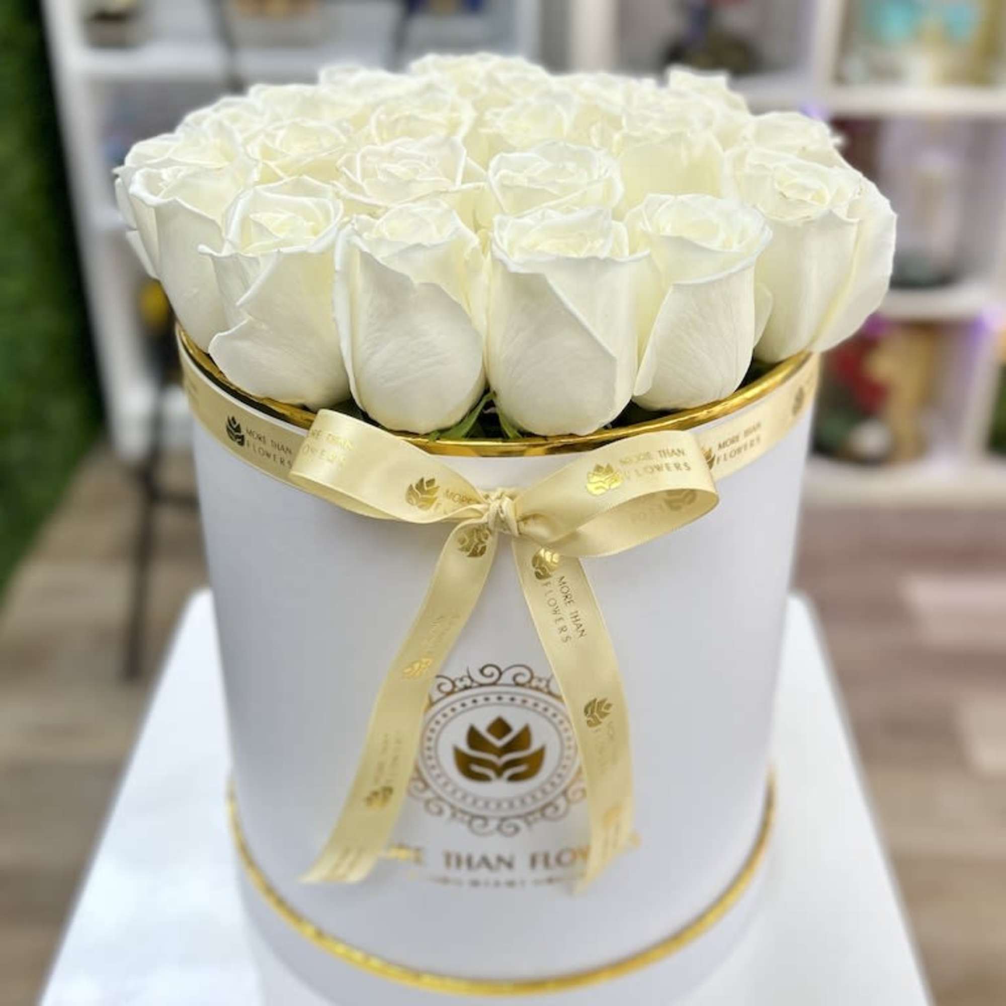 White roses arranged in a round white hat box with gold trim and bow