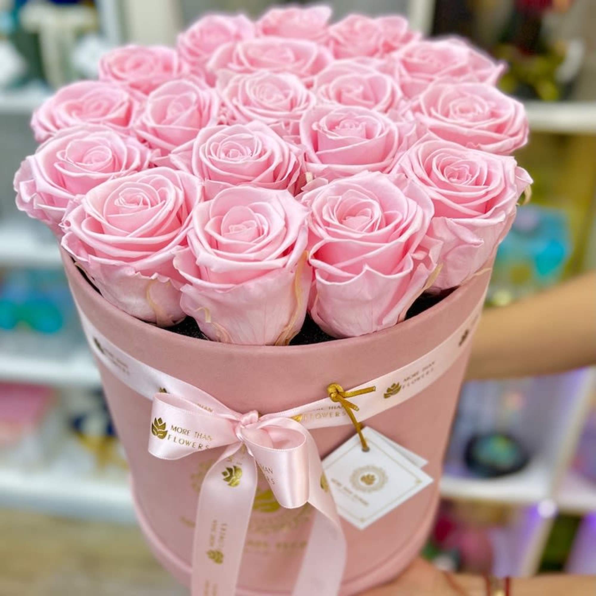 Round box of tightly arranged light pink roses with a pink ribbon and tag