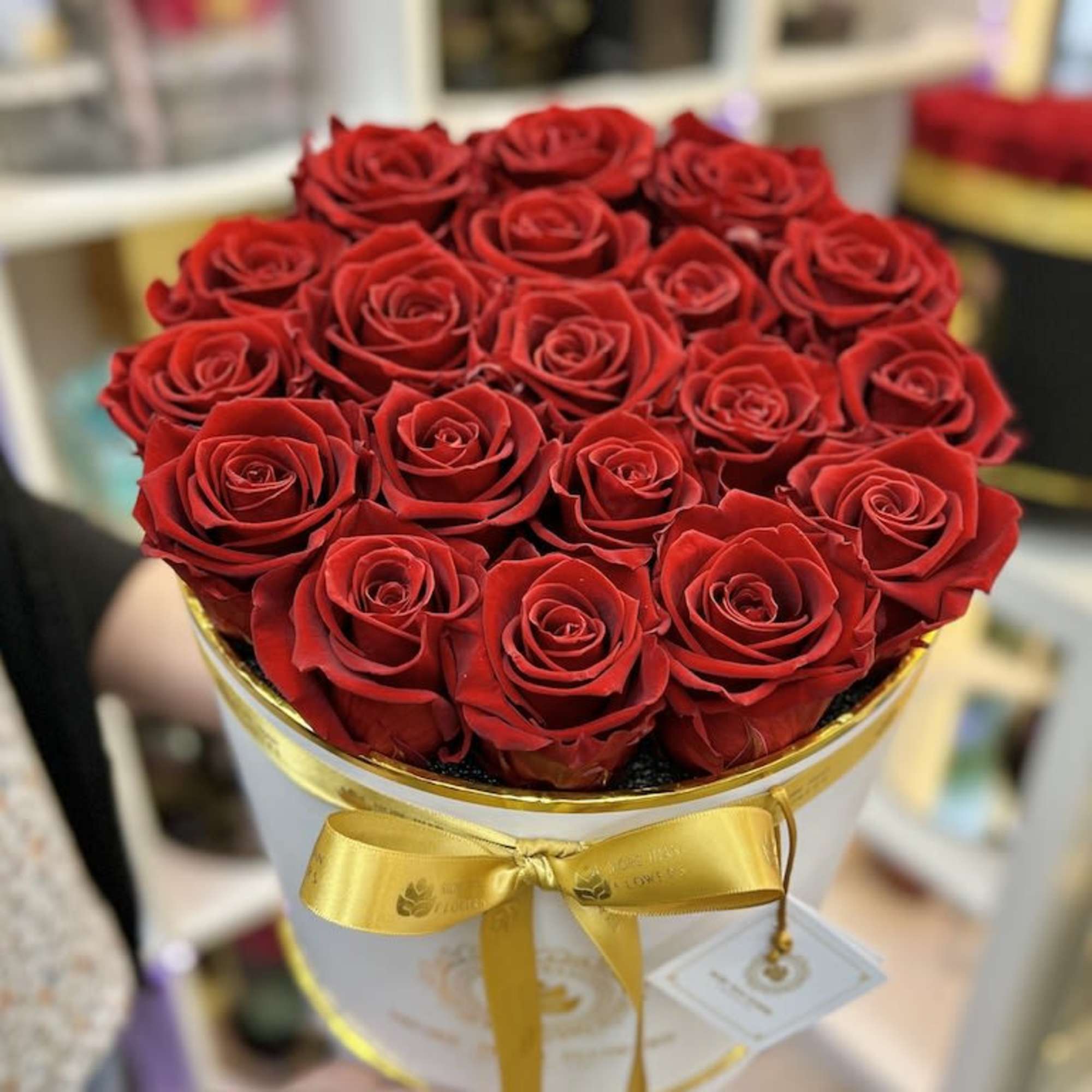 Round box of red roses with a gold ribbon held in someone’s hands
