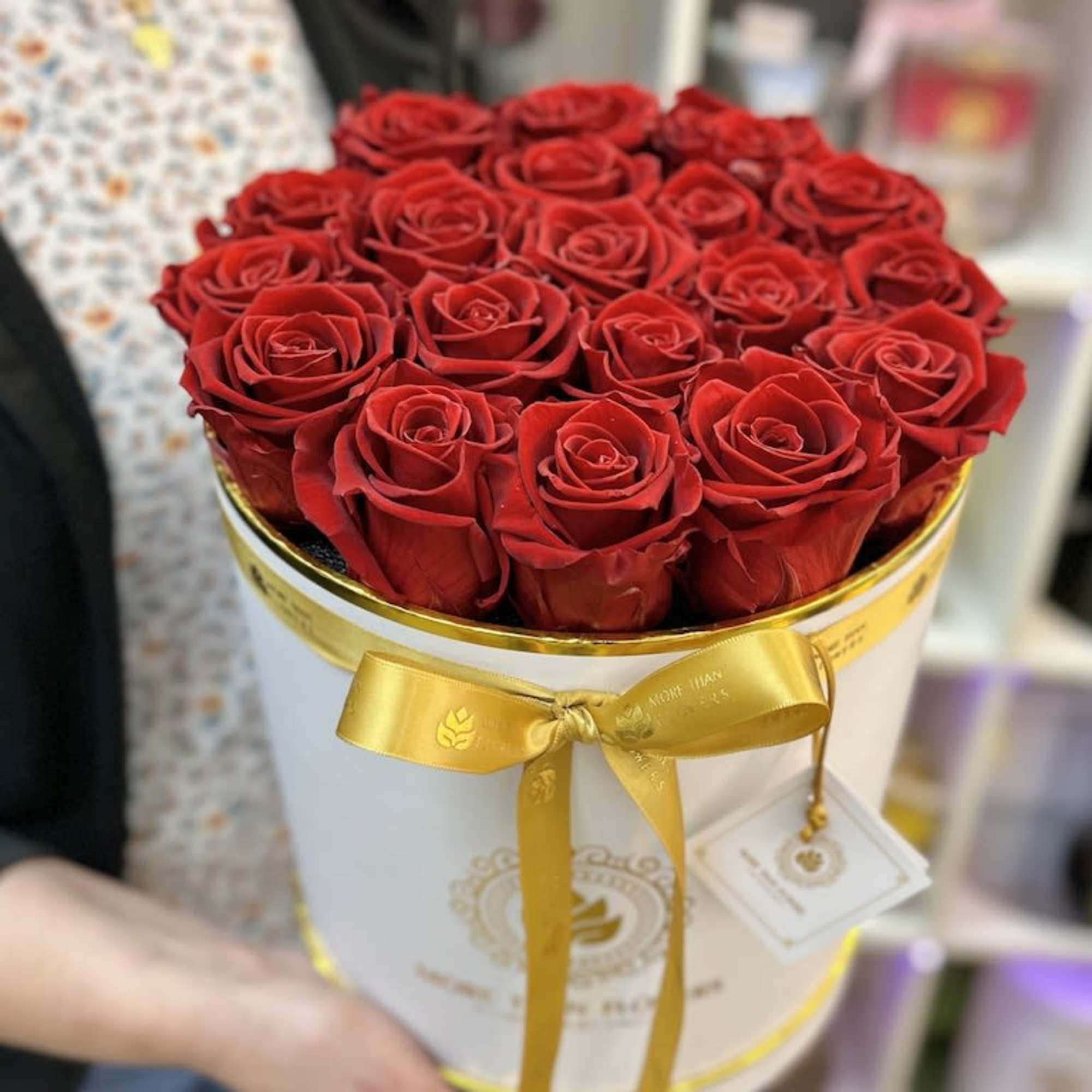 Round white hat box filled with tightly packed red roses and tied with a gold ribbon