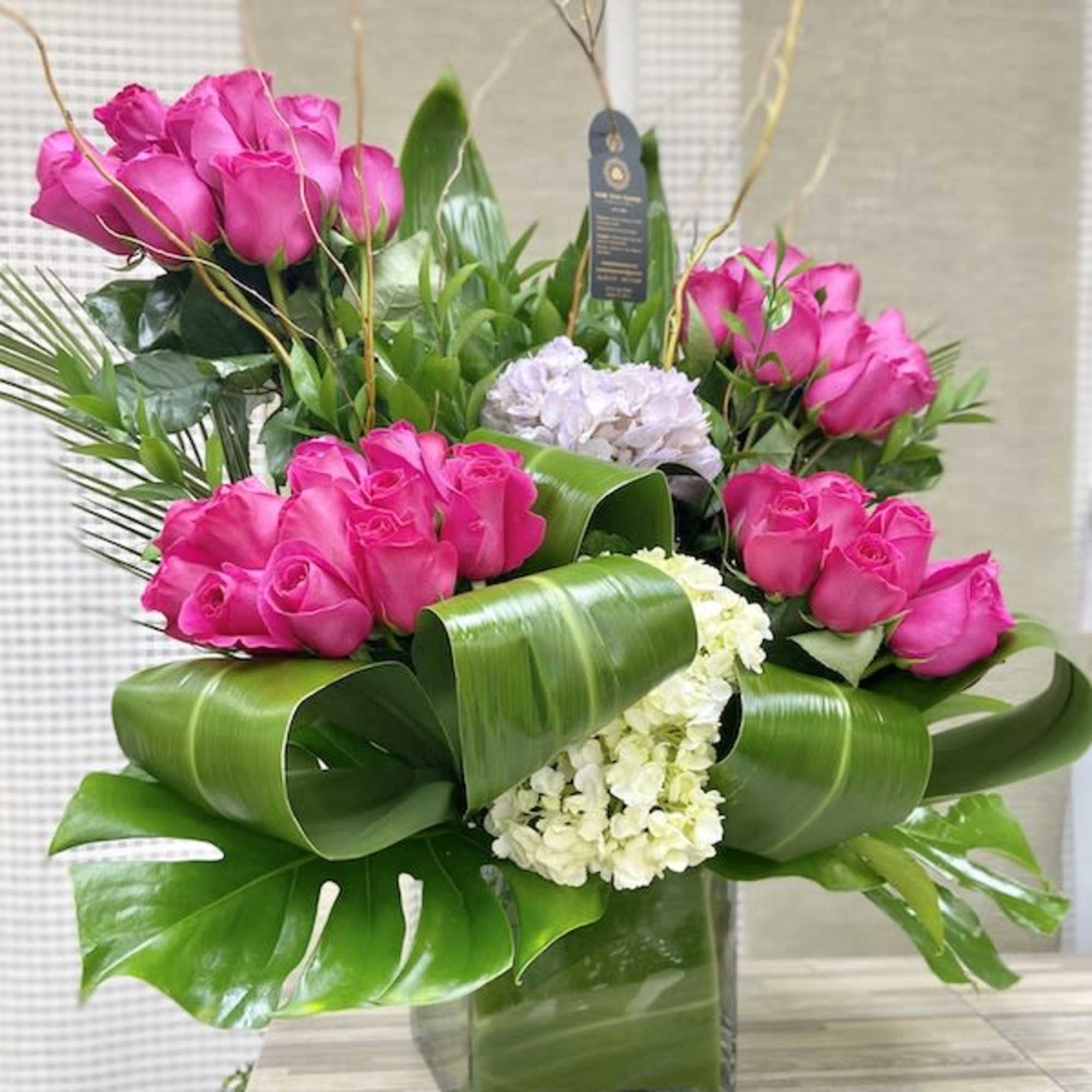 Modern arrangement of hot pink roses and white hydrangeas with large folded leaves in a square glass vase