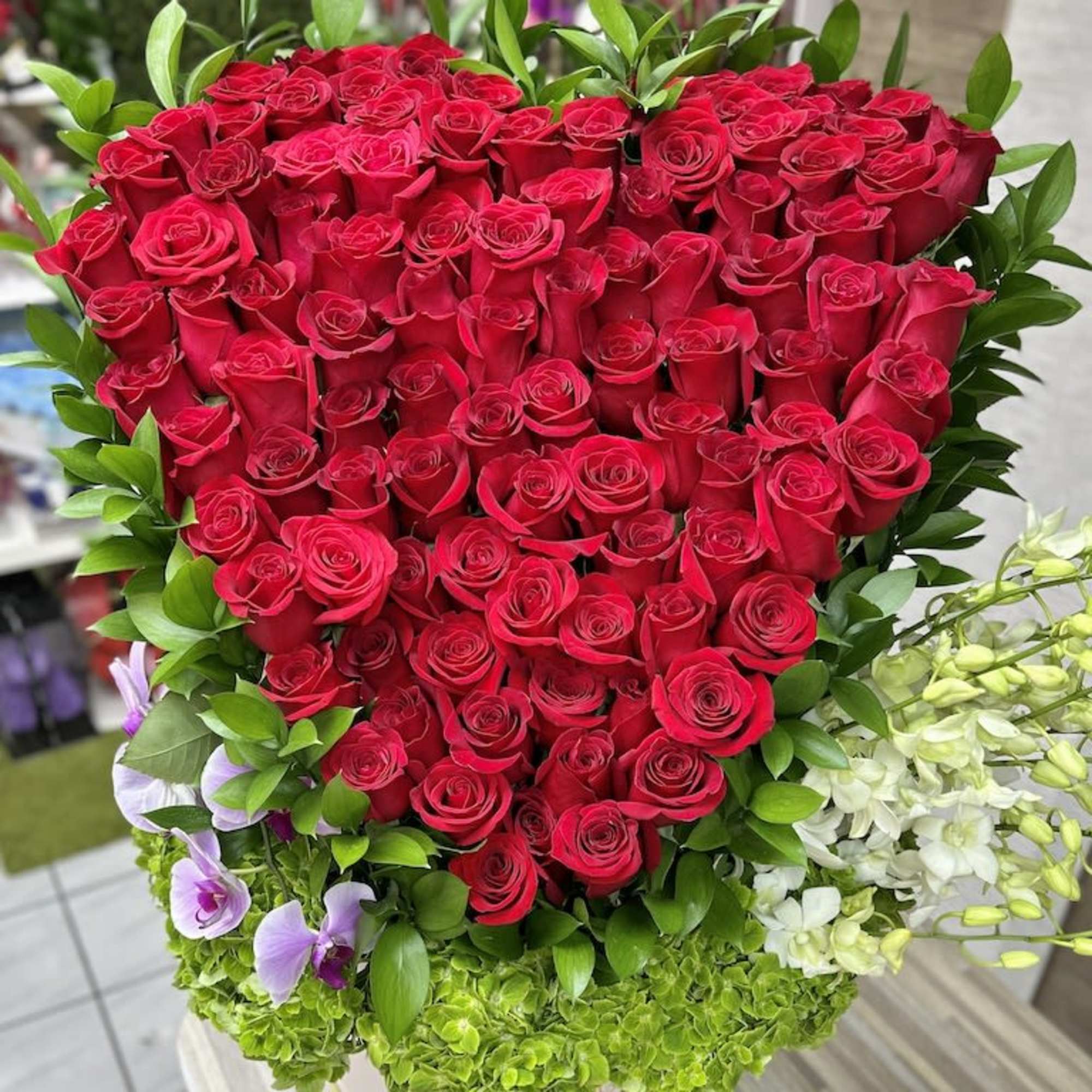 Heart-shaped arrangement of red roses with green hydrangeas and orchids in a white hatbox