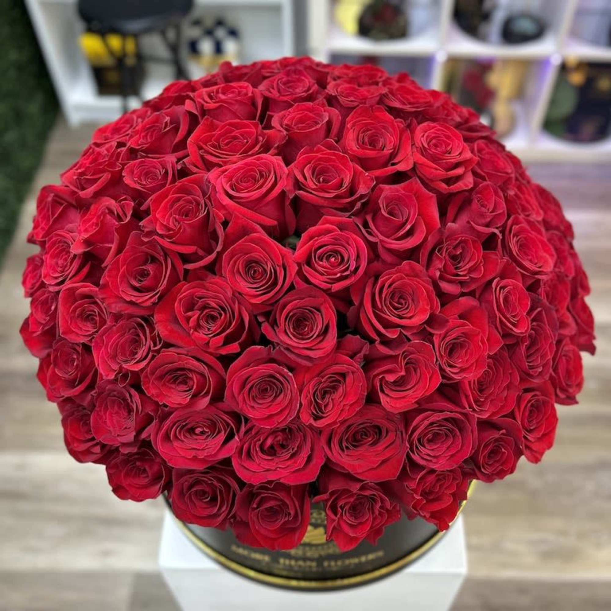 Round hatbox packed with many red roses on a white pedestal.