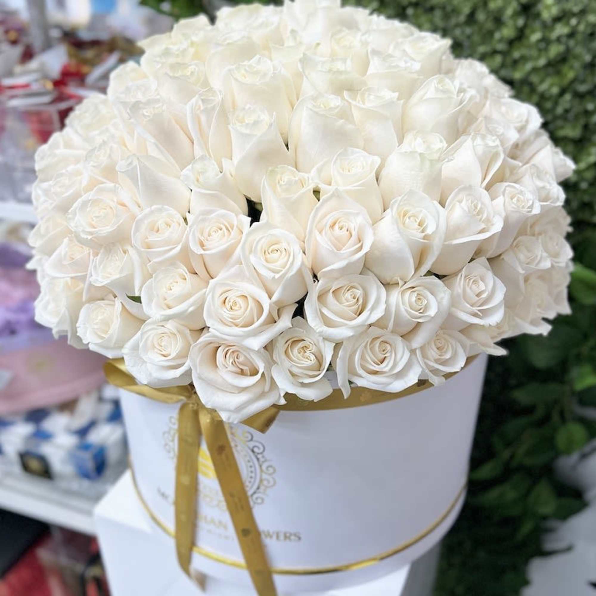 Large round hatbox of tightly packed white roses with a gold ribbon around the box