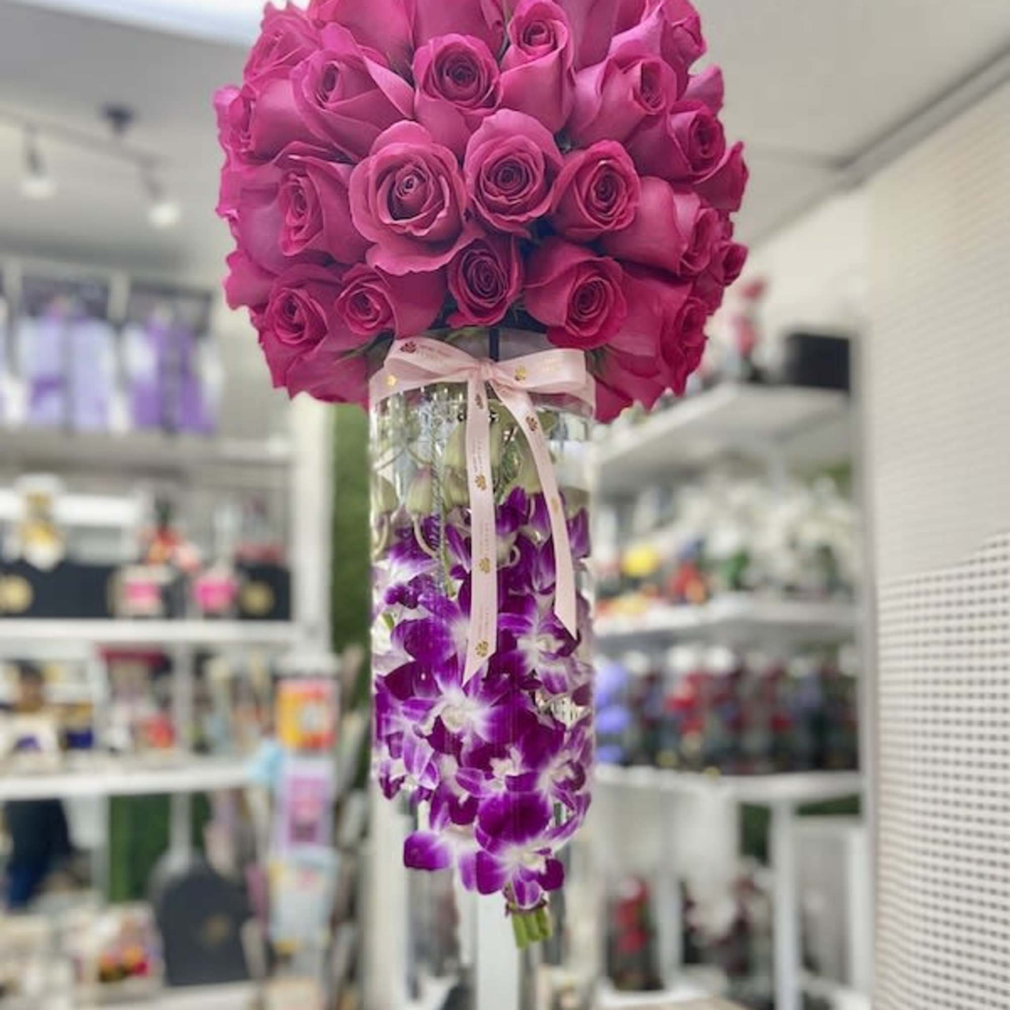 Tall glass vase with hot pink roses on top and submerged purple orchids tied with a ribbon.