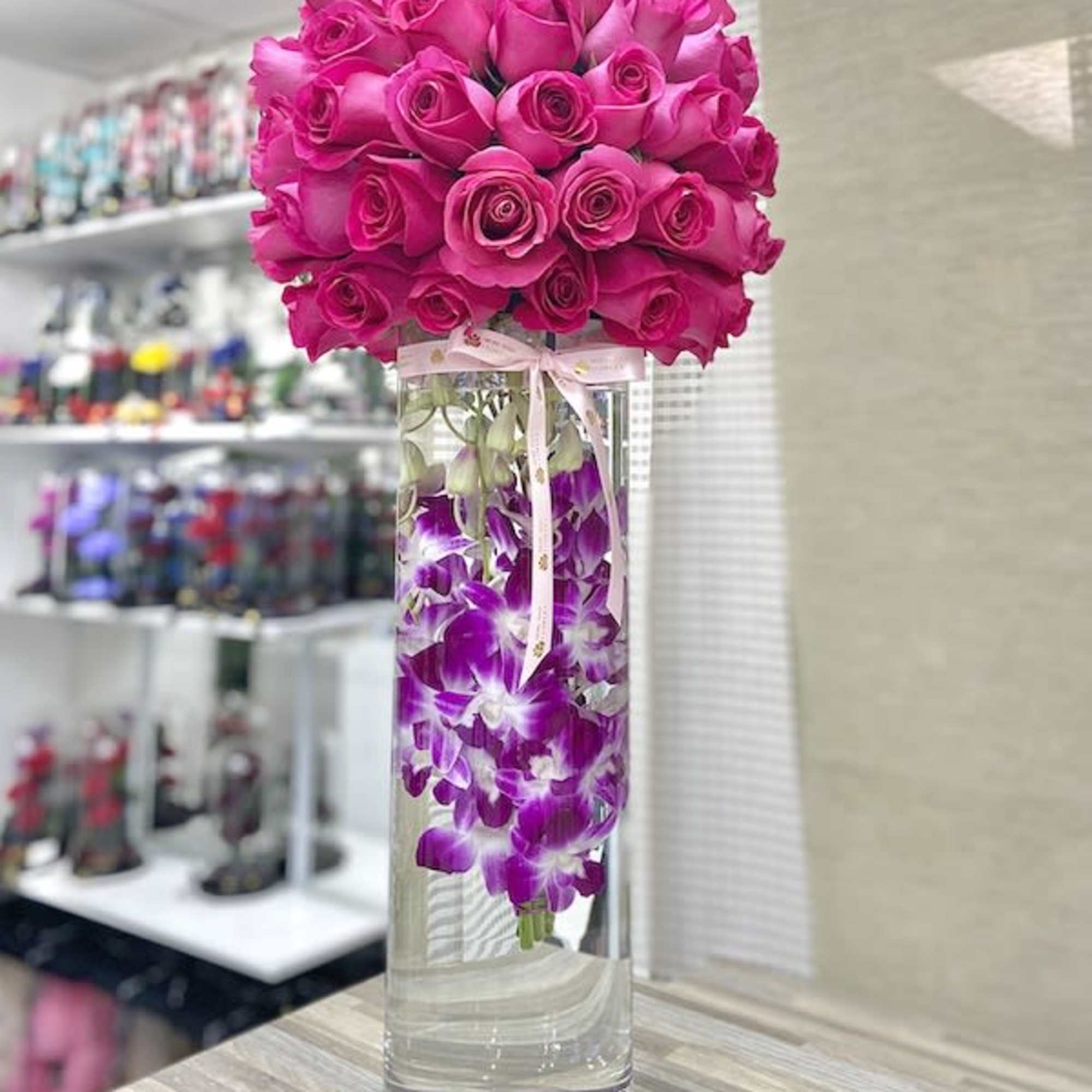 Tall cylinder vase with submerged purple orchids topped by a large dome of hot pink roses