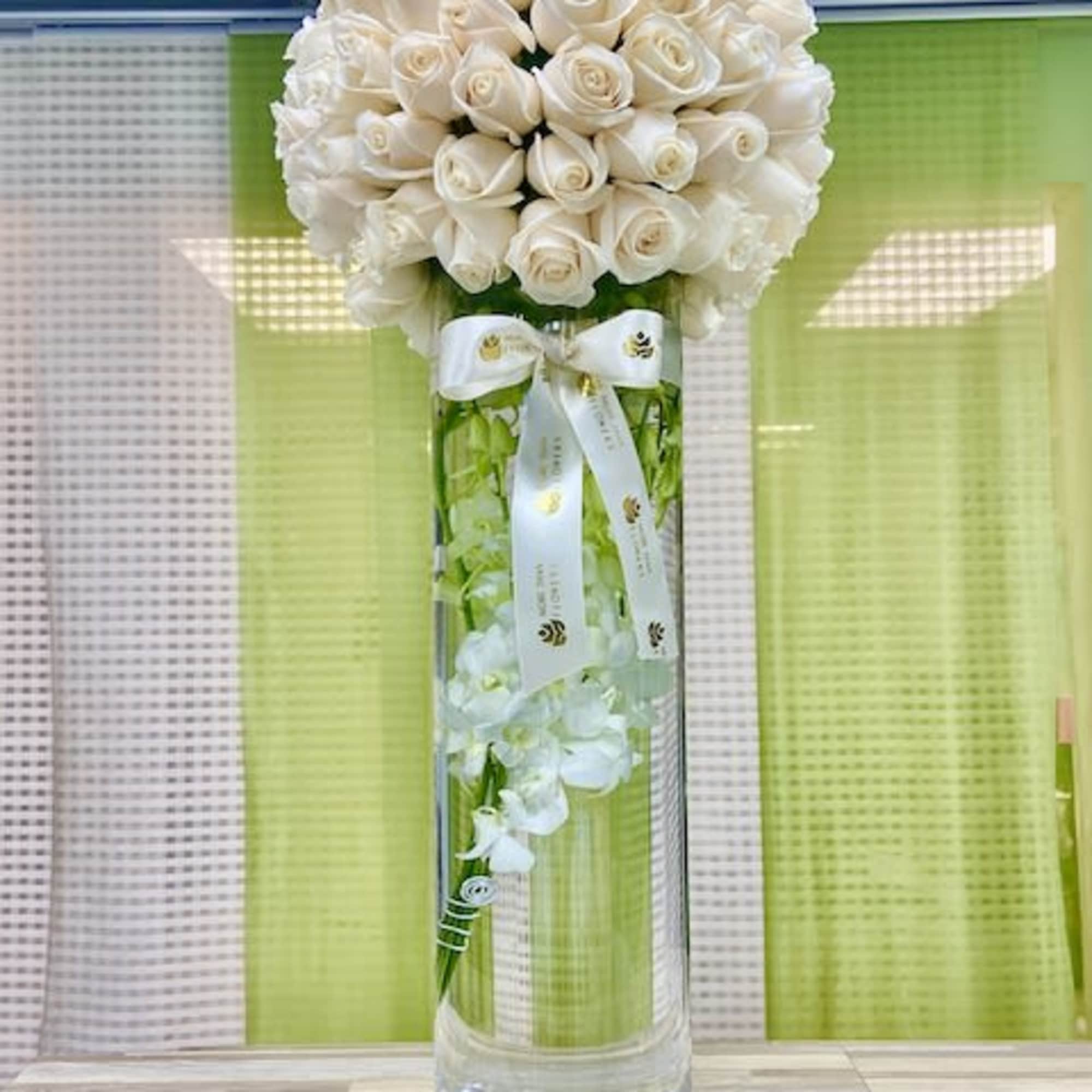 Tall glass cylinder vase with submerged white orchids topped by a dense dome of ivory roses and ribbon.