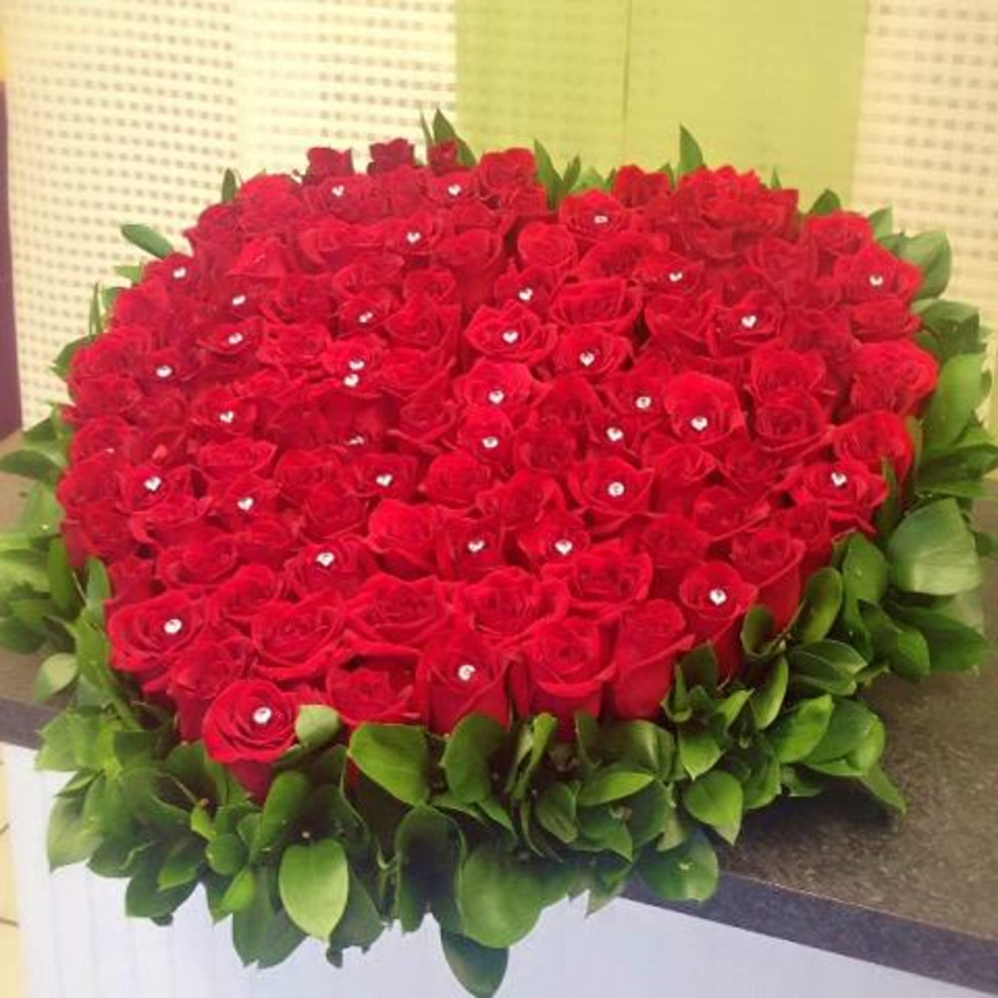 Heart-shaped arrangement of red roses with jeweled centers edged in glossy green leaves