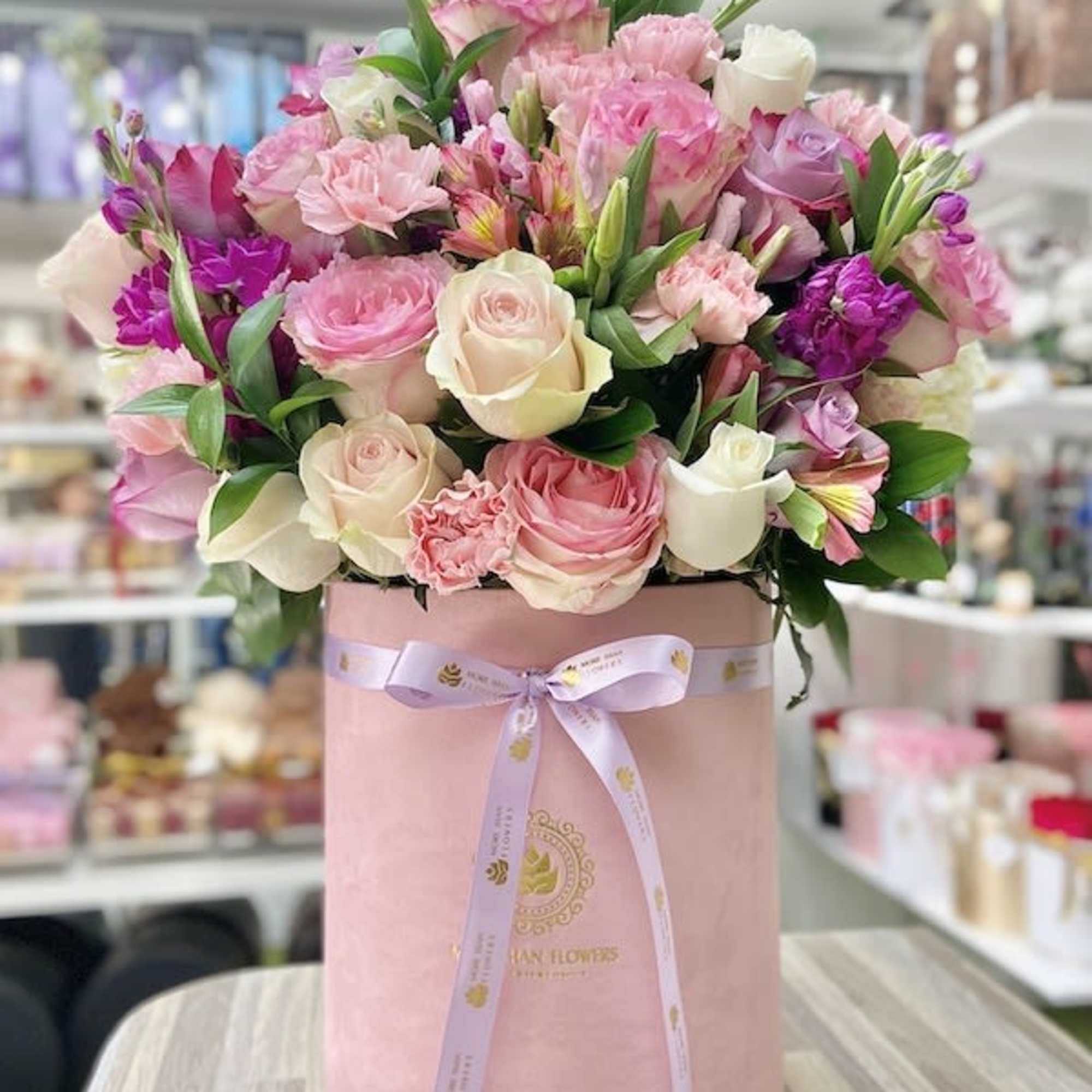 Pink and cream roses with mixed pink blooms arranged in a pink hatbox with a ribbon bow.