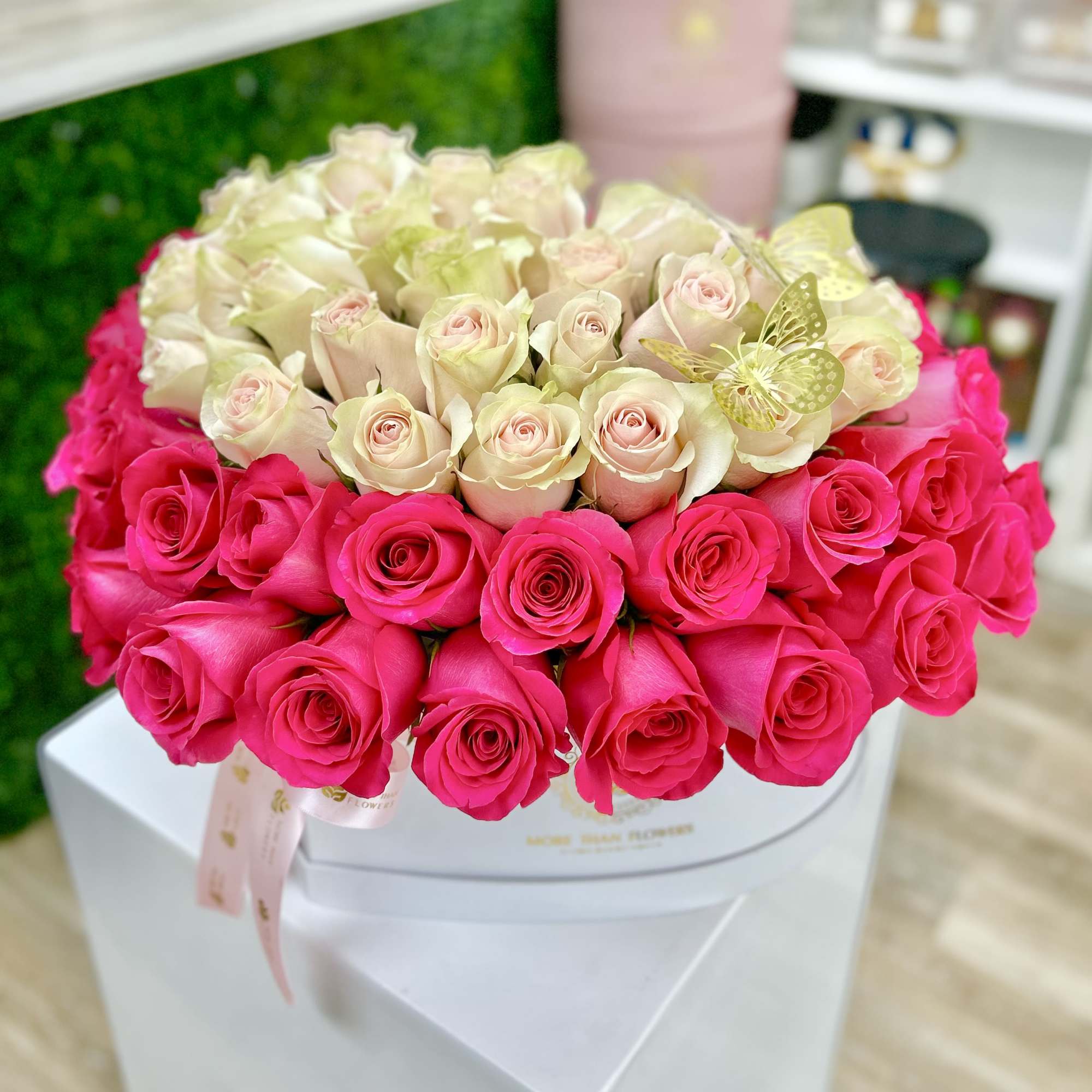 Round box arrangement of hot pink and pale cream roses with a decorative butterfly.