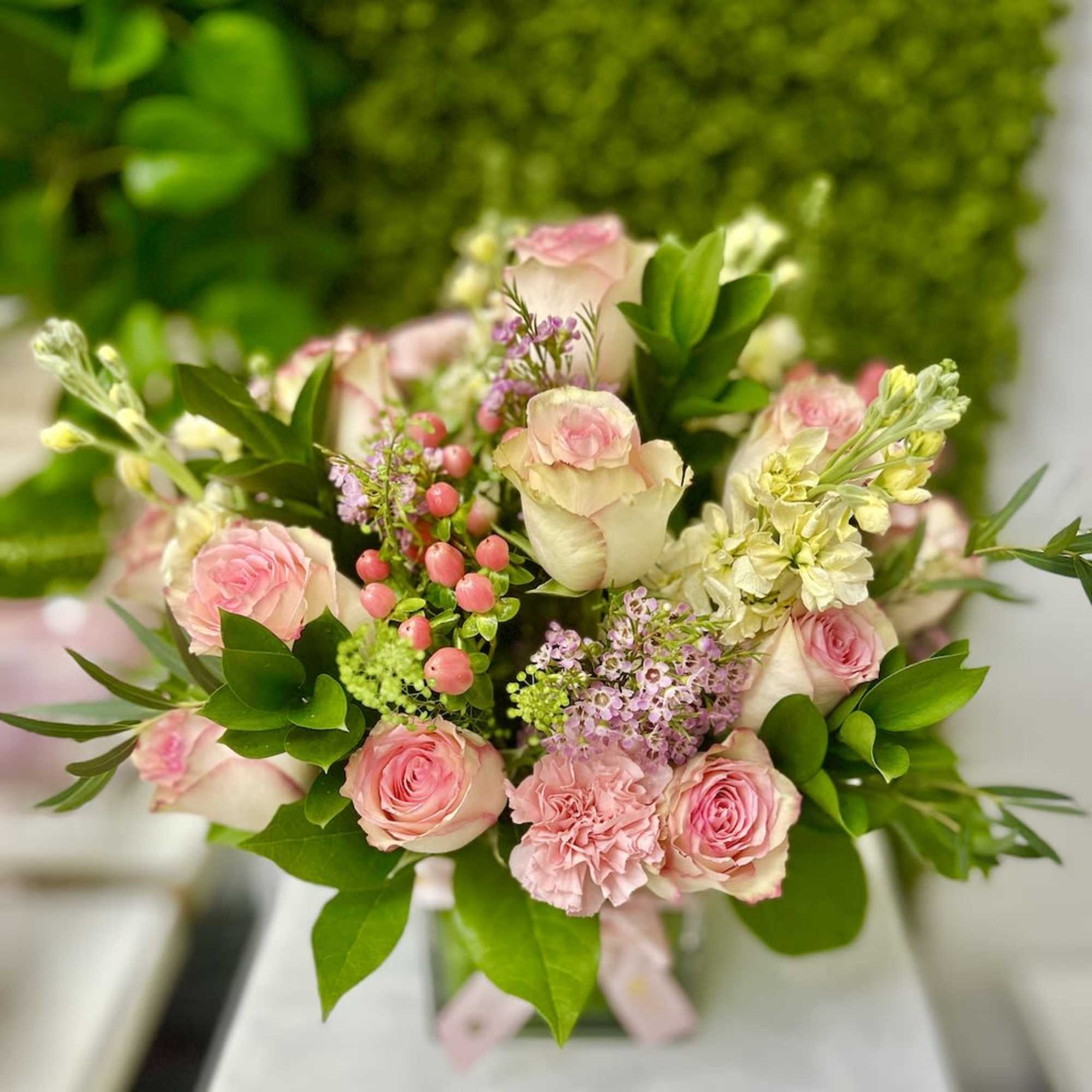 Arrangement of pink roses and carnations with ivory blooms and berries in a clear glass vase