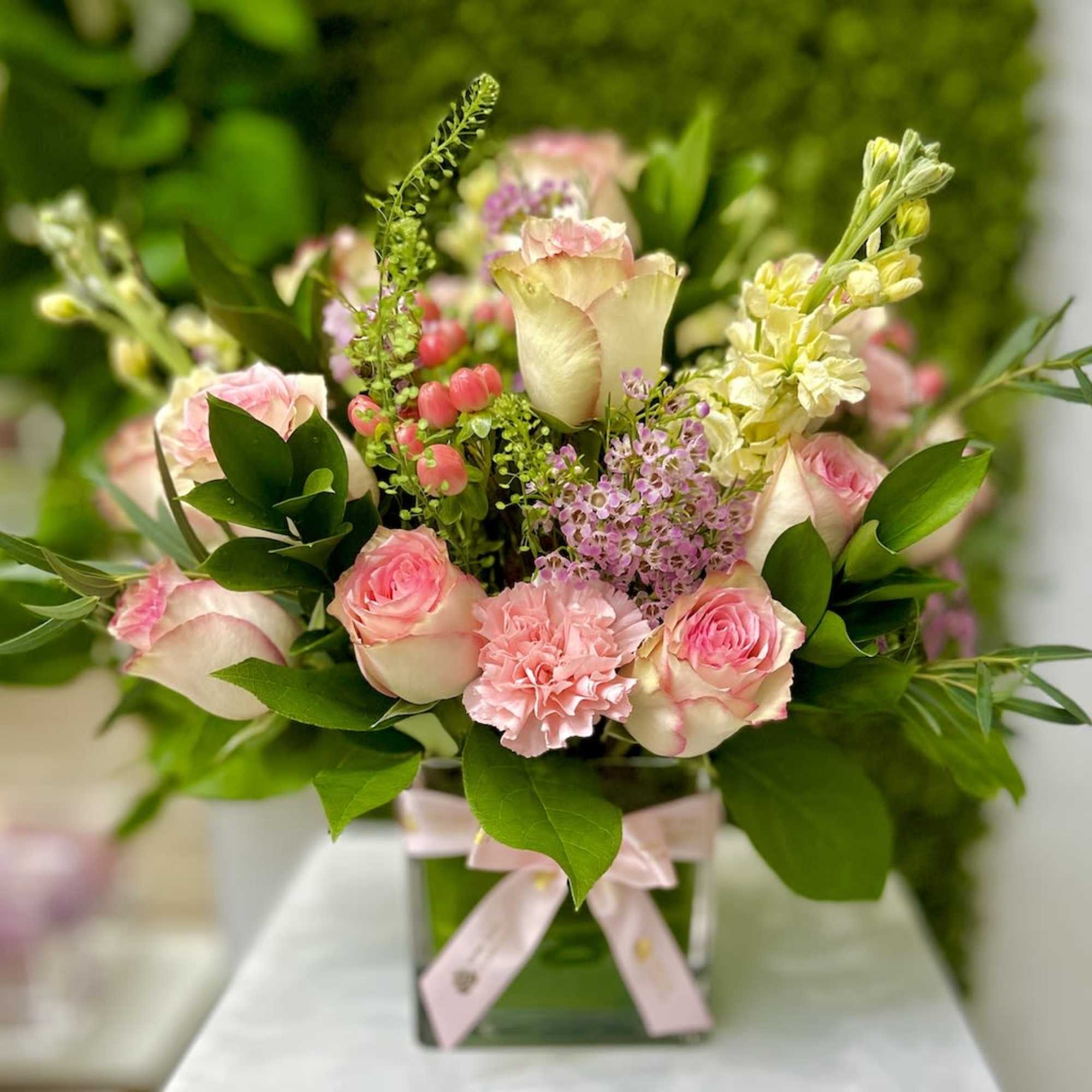 Pink and cream flower arrangement in a glass cube vase with a pink ribbon bow