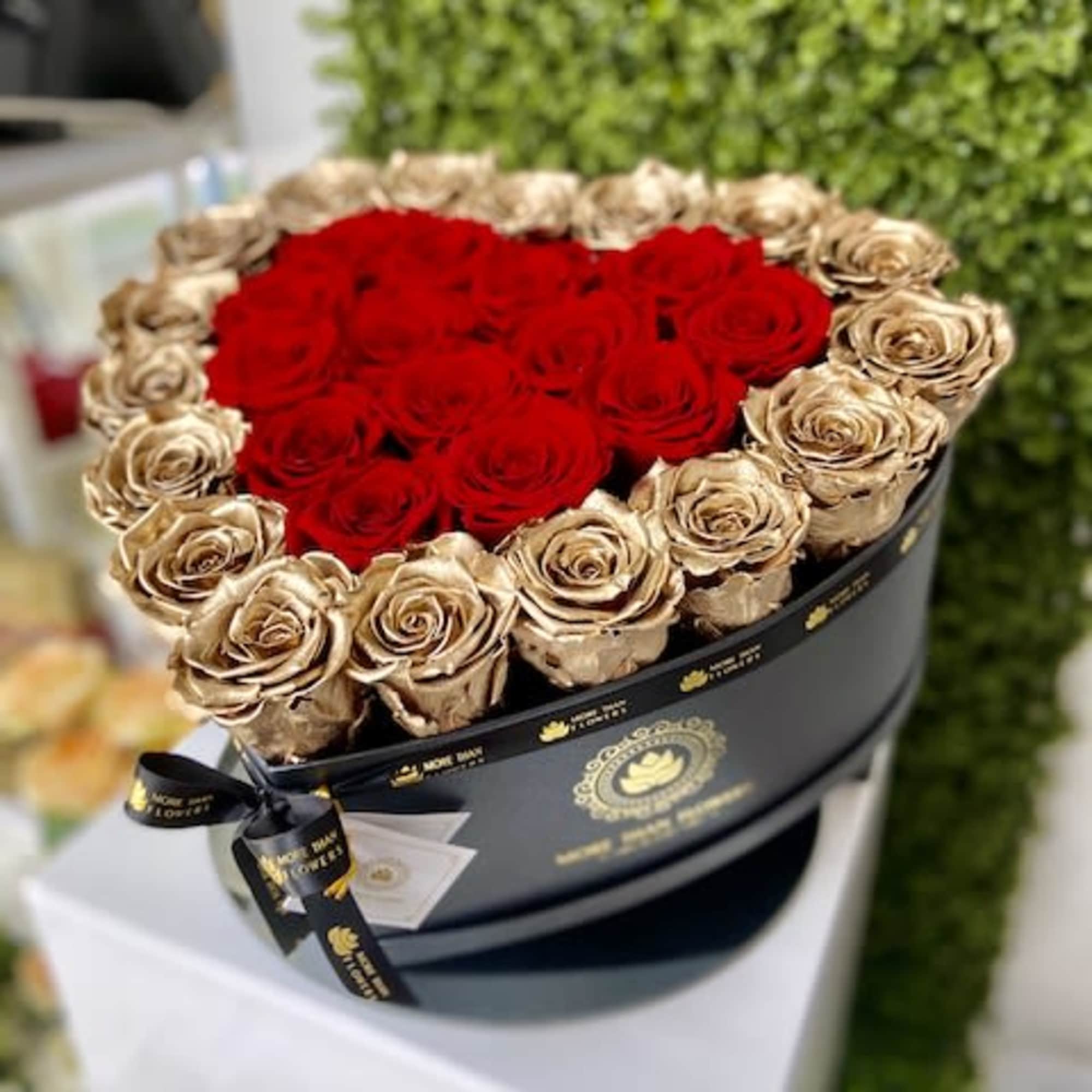 Round black hatbox of red and gold roses with red blooms shaped into a heart.