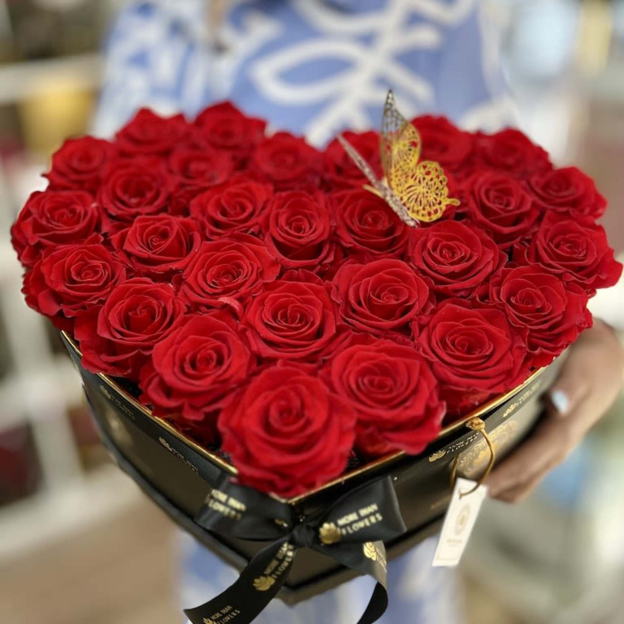 Heart-shaped black box filled with red roses and a decorative gold butterfly accent.
