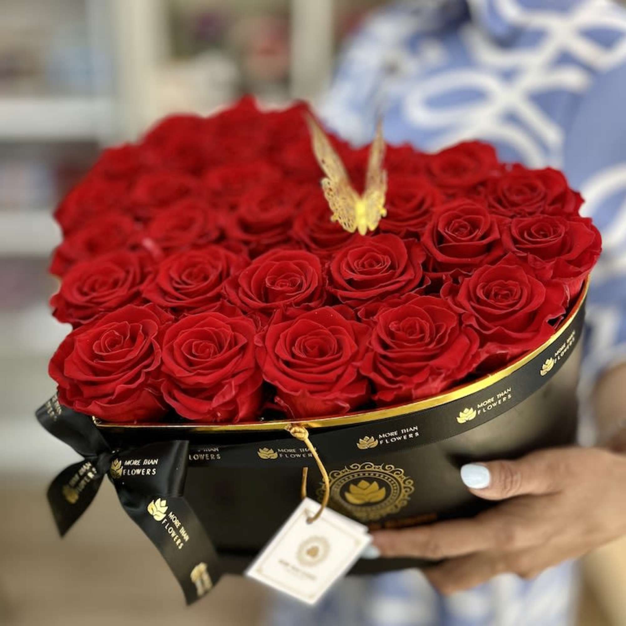 Heart-shaped black box filled with red roses and a gold butterfly accent, held in someone’s hands.