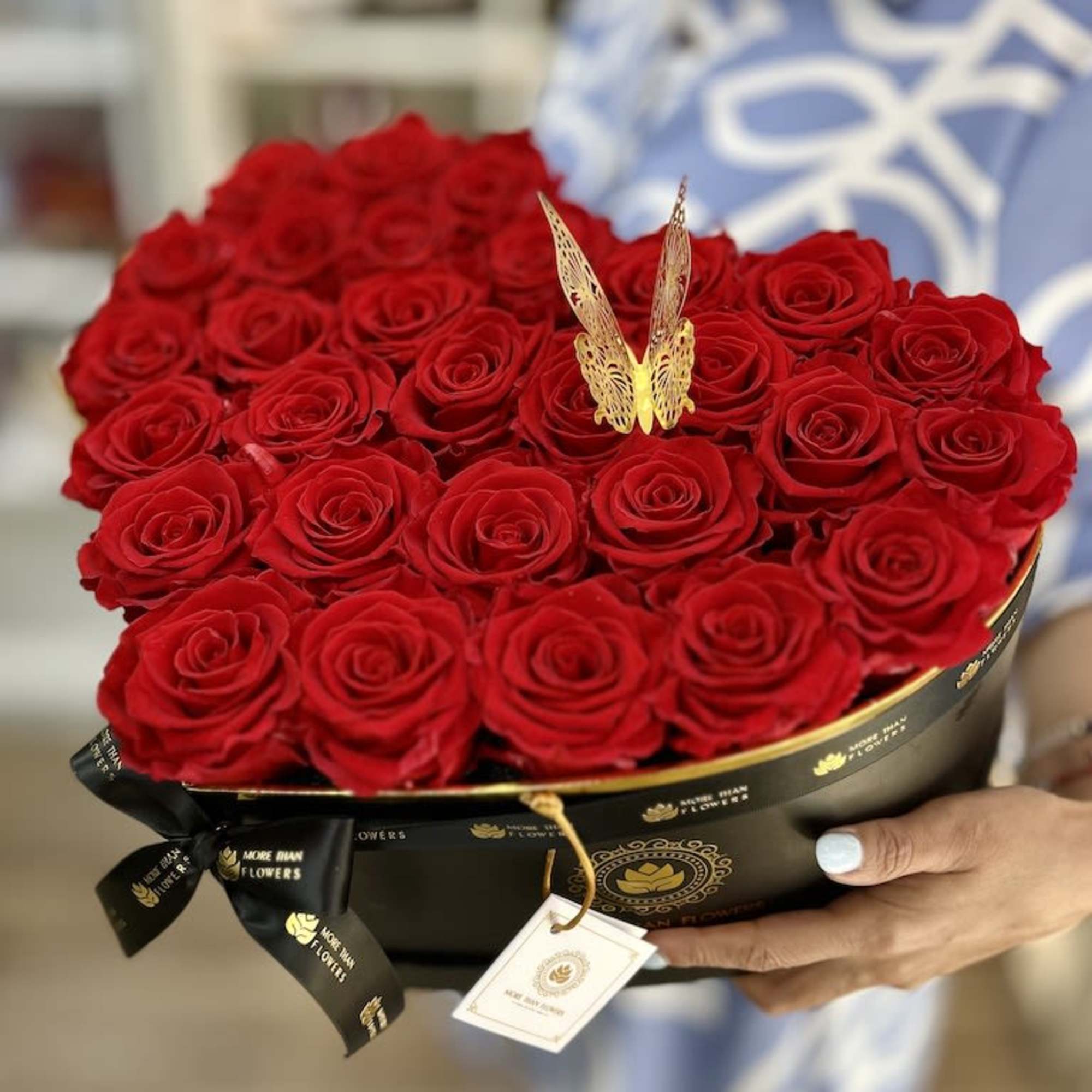 Heart-shaped black box filled with red roses and a gold butterfly accent held in someone's hands