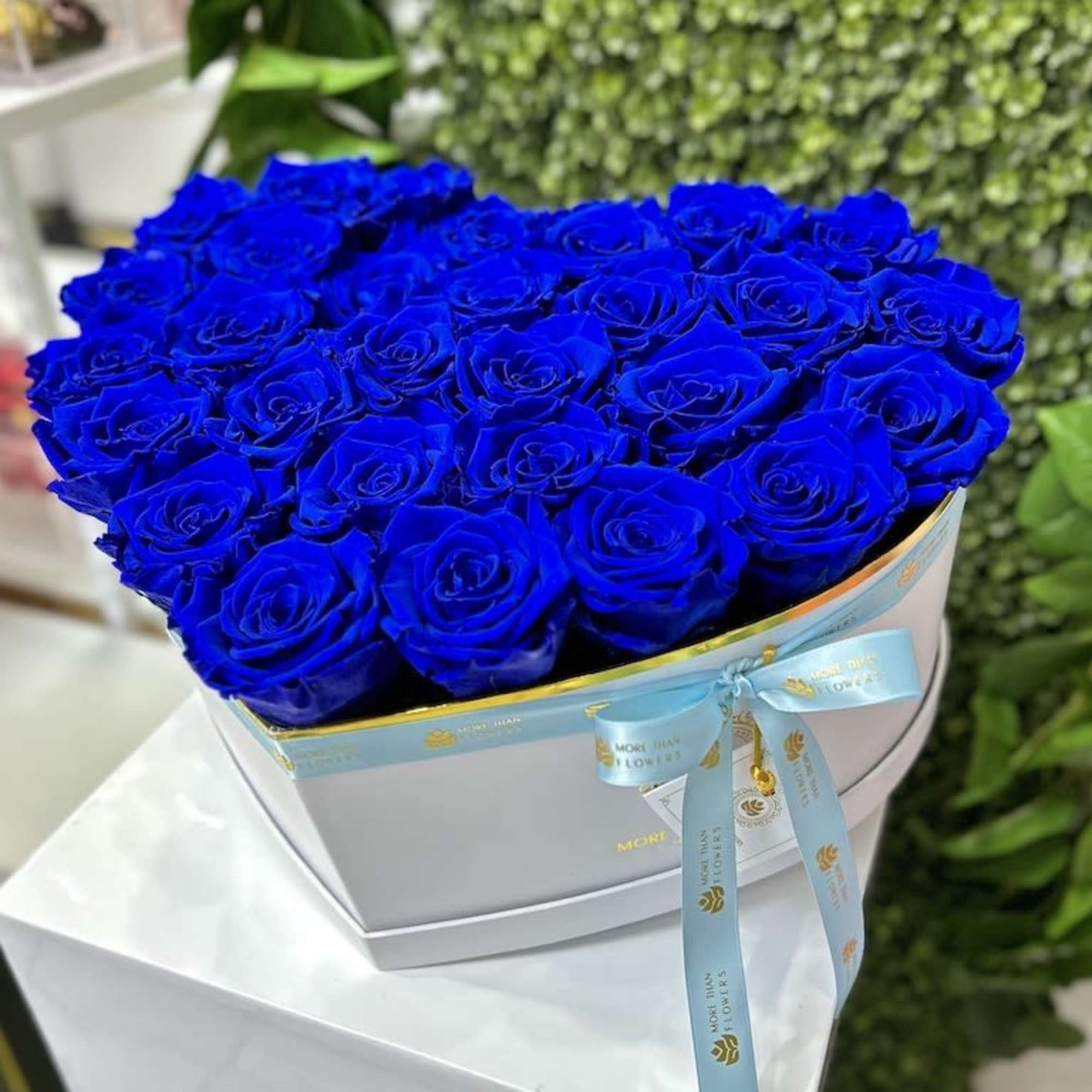 Heart-shaped box of vivid blue roses with a ribbon on a white pedestal