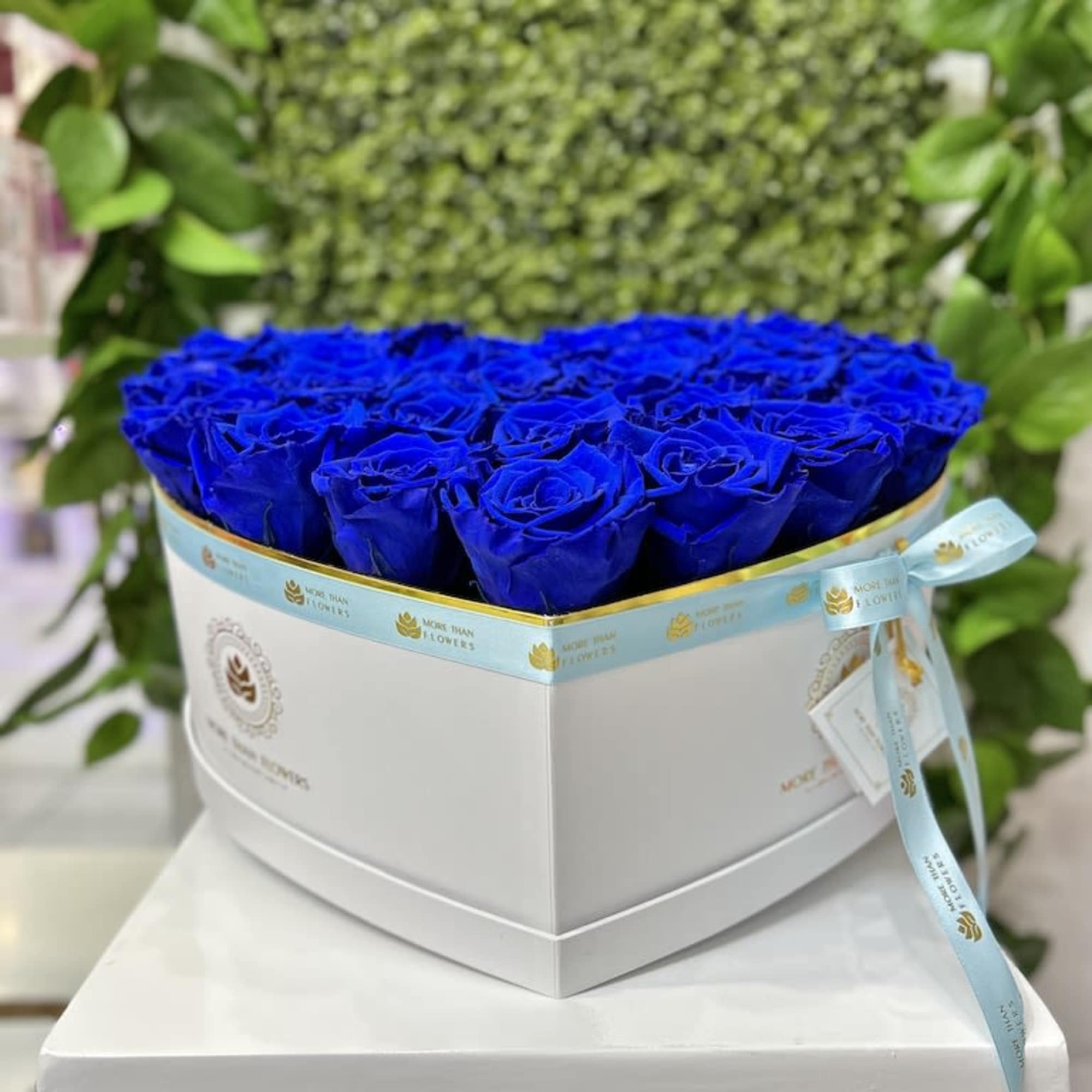 Heart-shaped white box filled with vivid blue roses and tied with a light blue ribbon