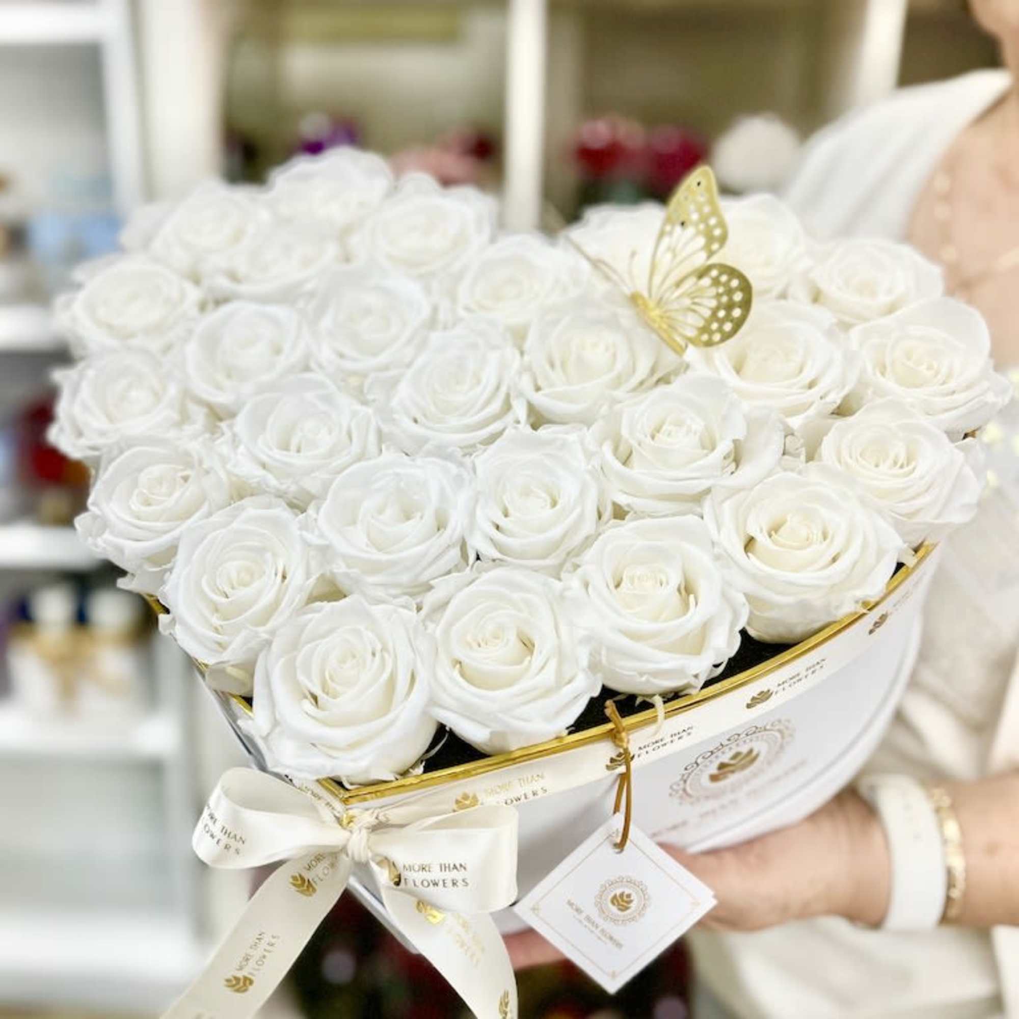 Heart-shaped box of white roses with gold butterfly accent held in both hands