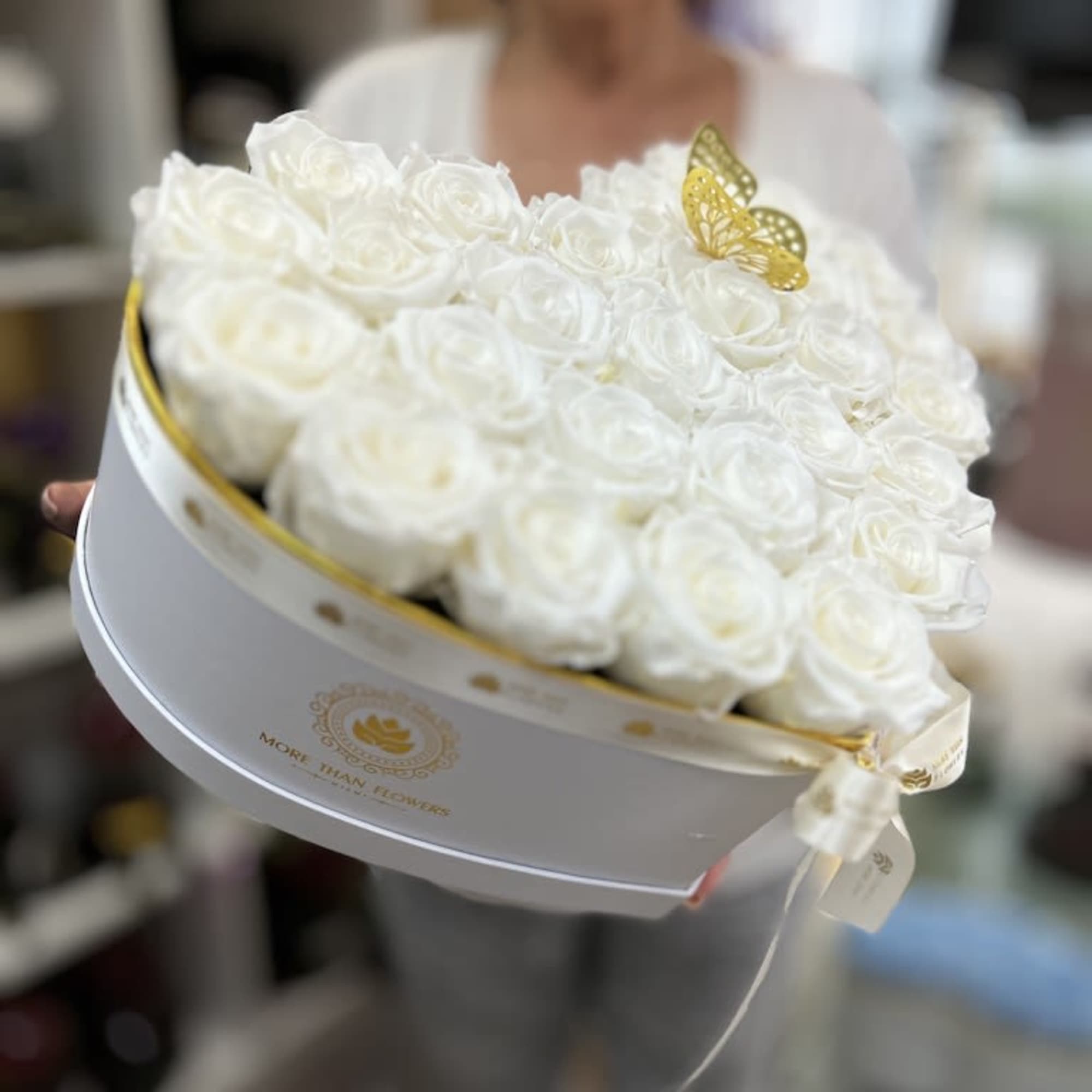 White hatbox filled with white roses and topped with a small gold butterfly decoration