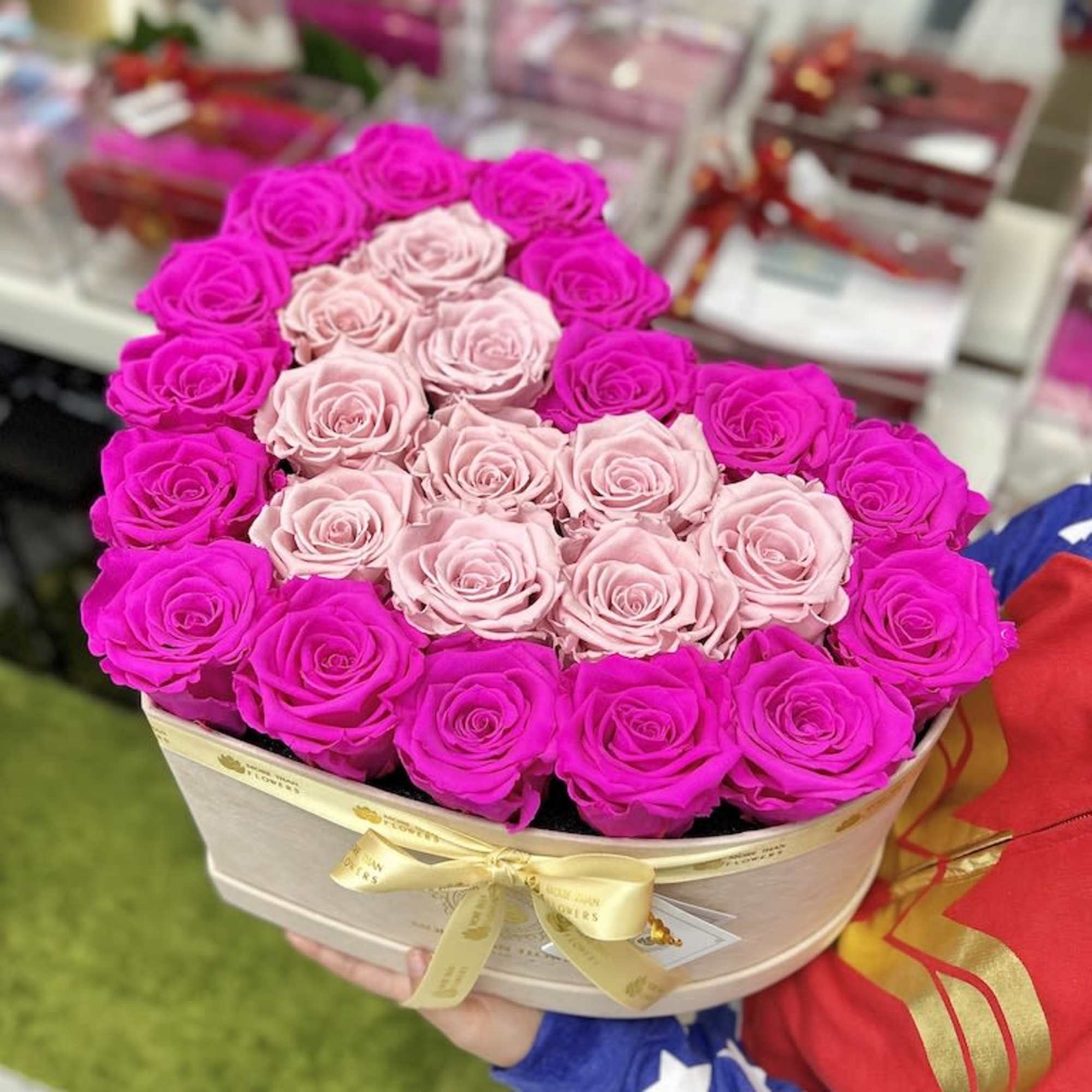 Heart-shaped box of hot pink and pale pink roses held in both hands