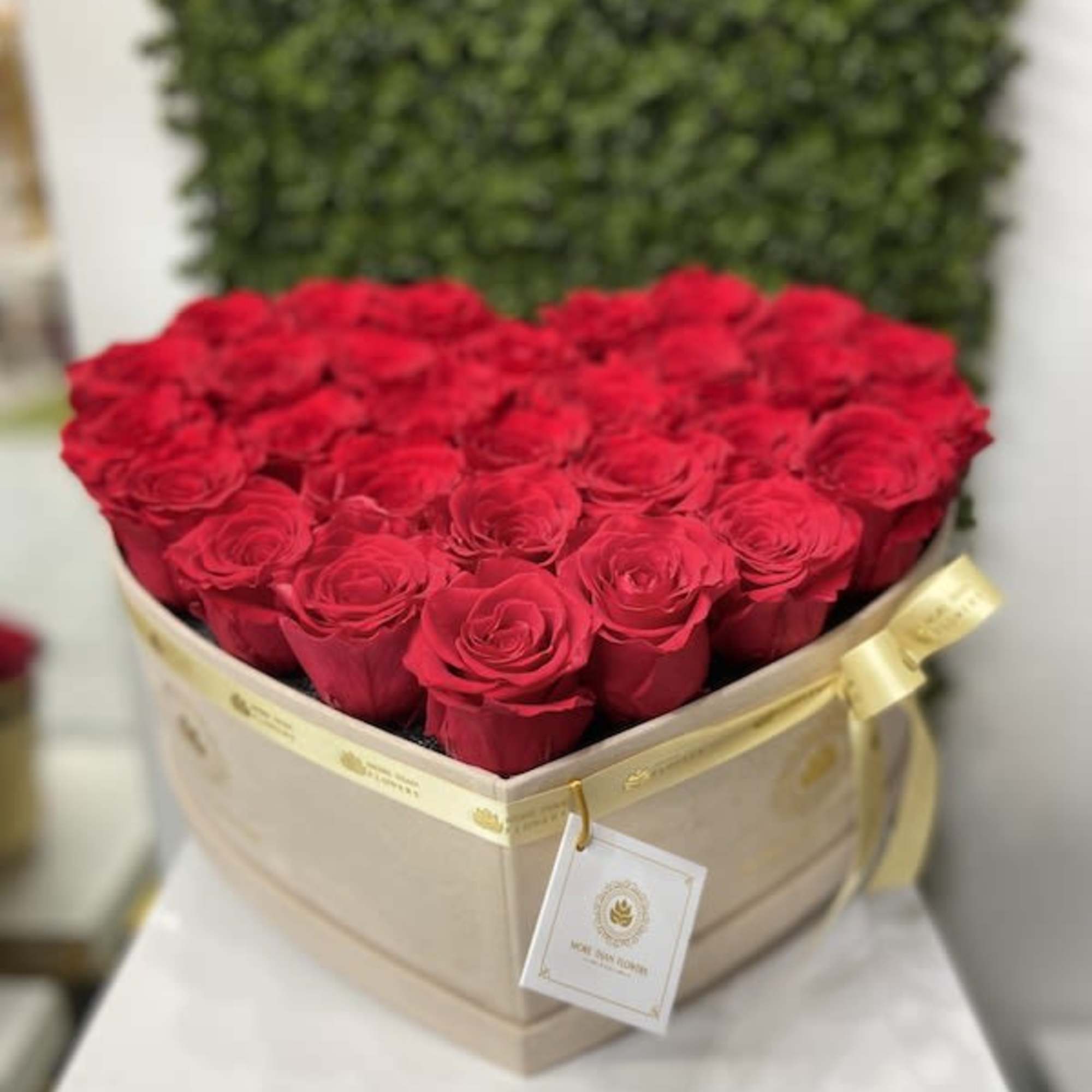 Heart-shaped box filled with tightly packed red roses and a gold ribboned tag.