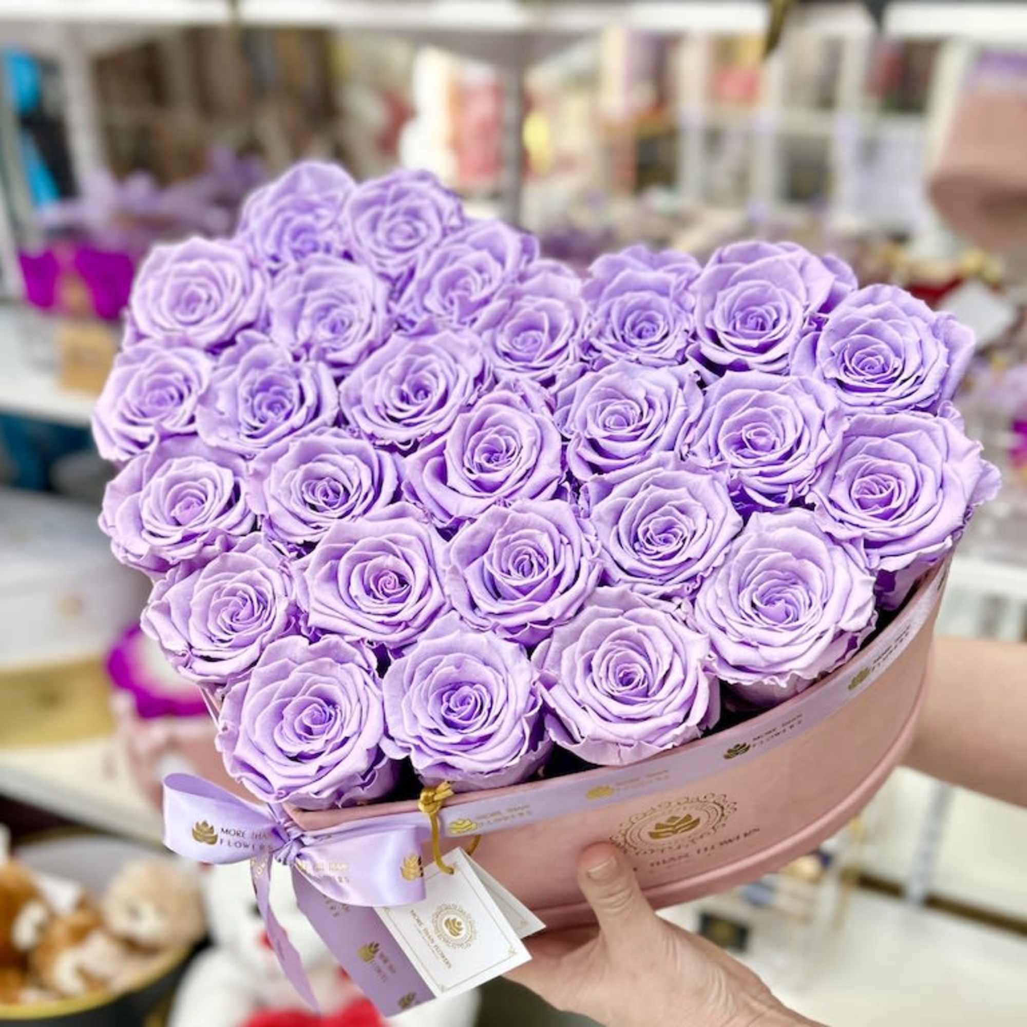 Heart-shaped box filled with tightly packed lavender roses held in both hands