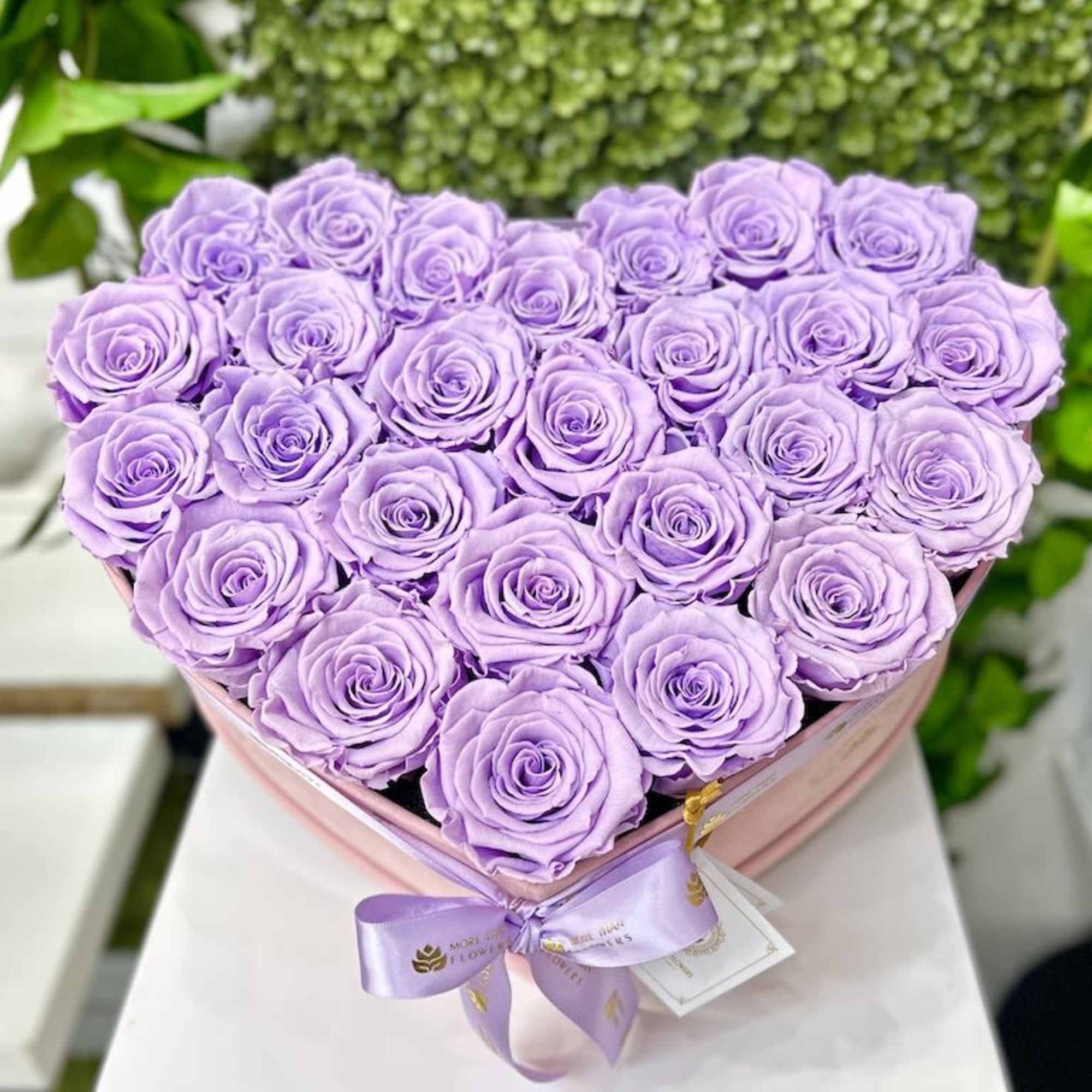 Heart-shaped box of lavender roses with satin ribbon bow on a white surface