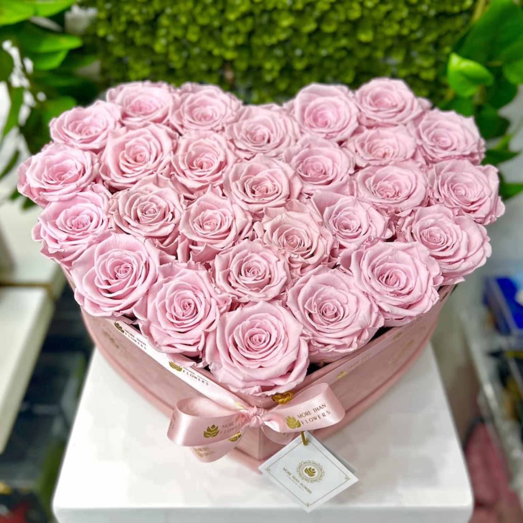 Heart-shaped pink box filled with pale pink roses and tied with a ribbon.