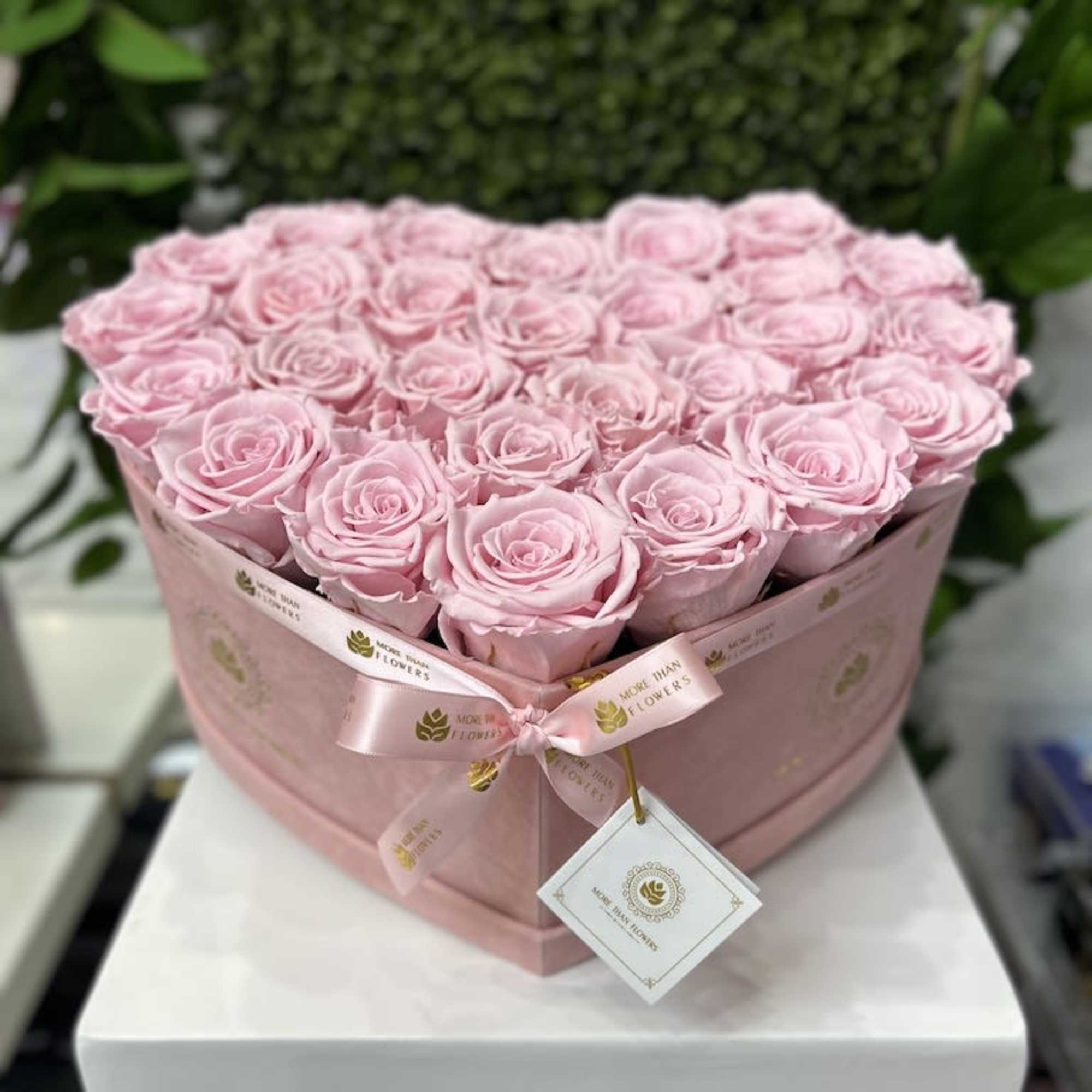 Heart-shaped box of light pink roses with ribbon on a white pedestal