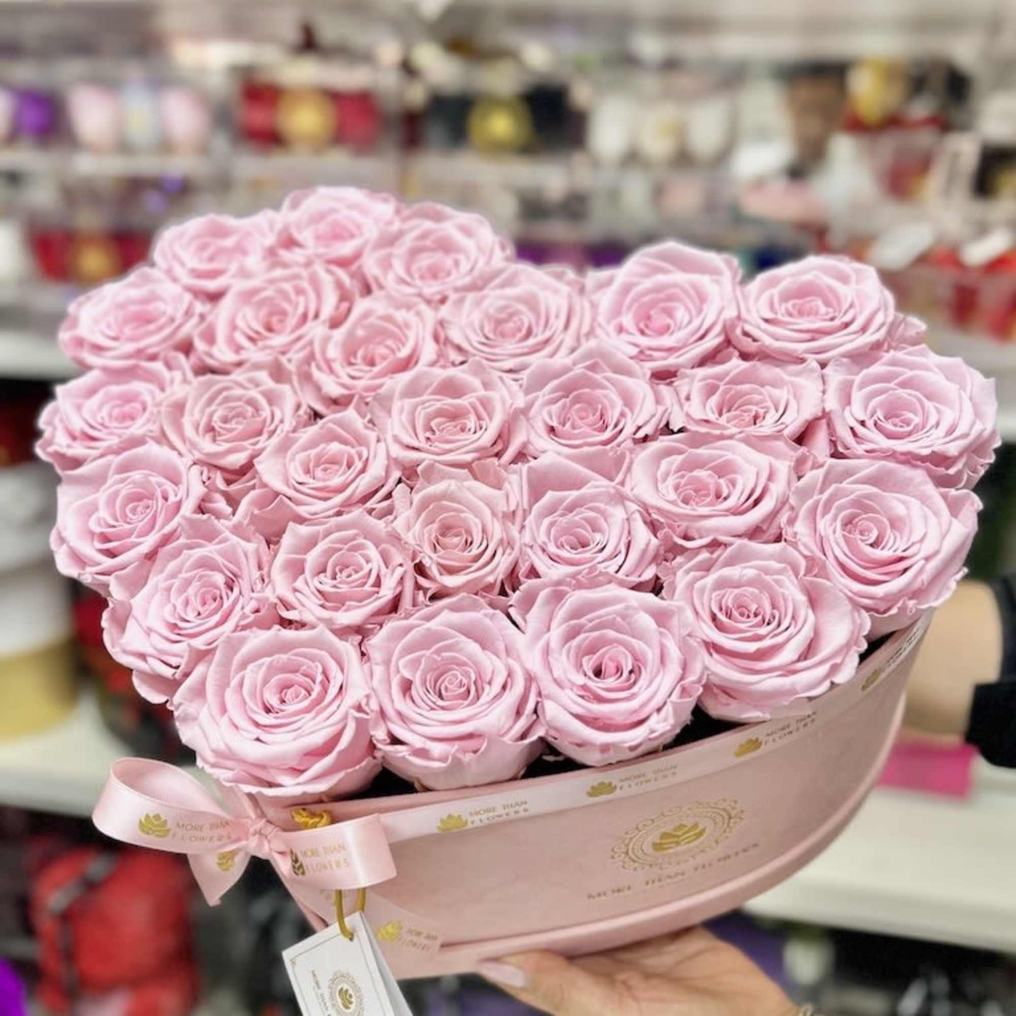 Heart-shaped arrangement of light pink roses in a pink hat box with ribbon.