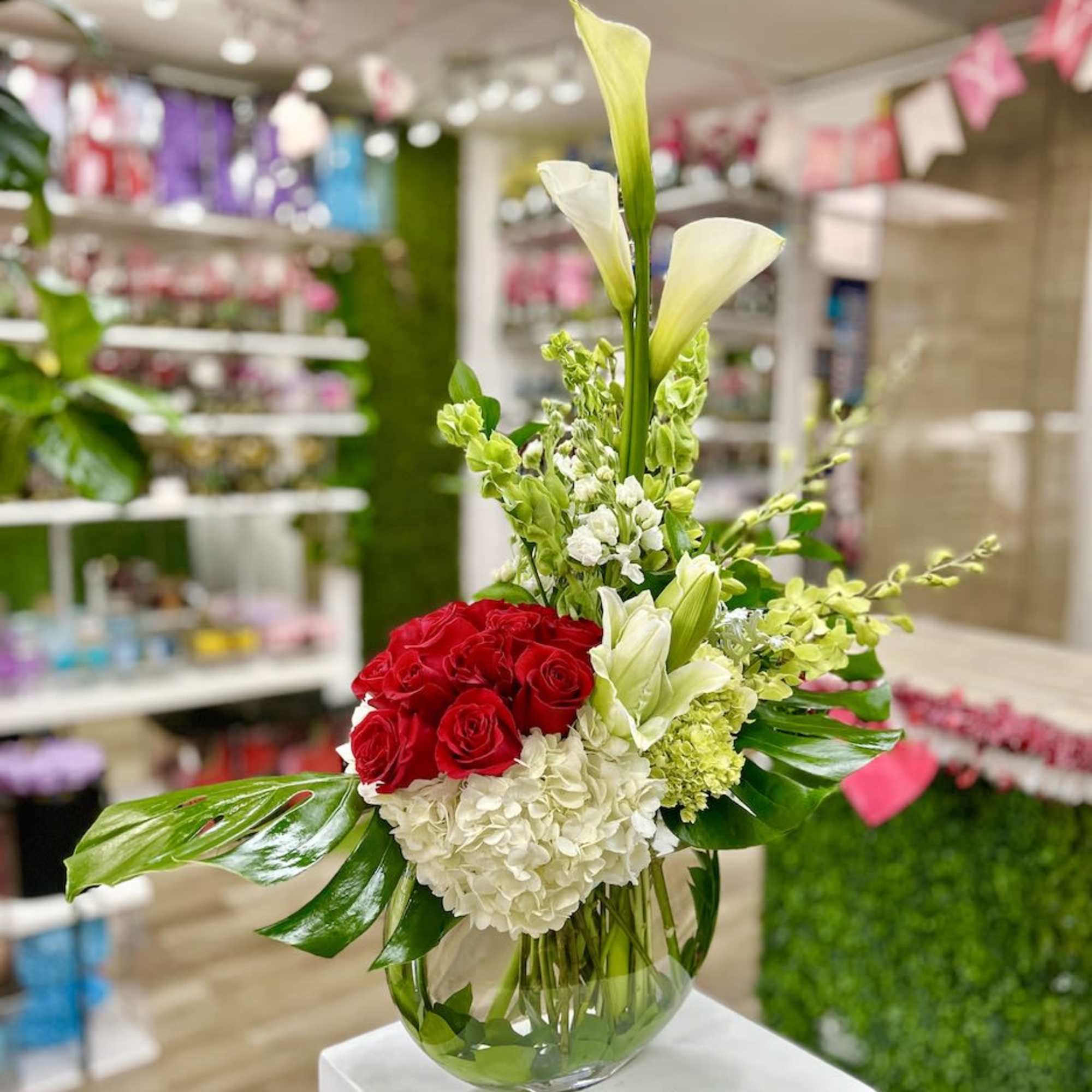 Modern arrangement of red roses, white calla lilies and hydrangea in a round glass vase