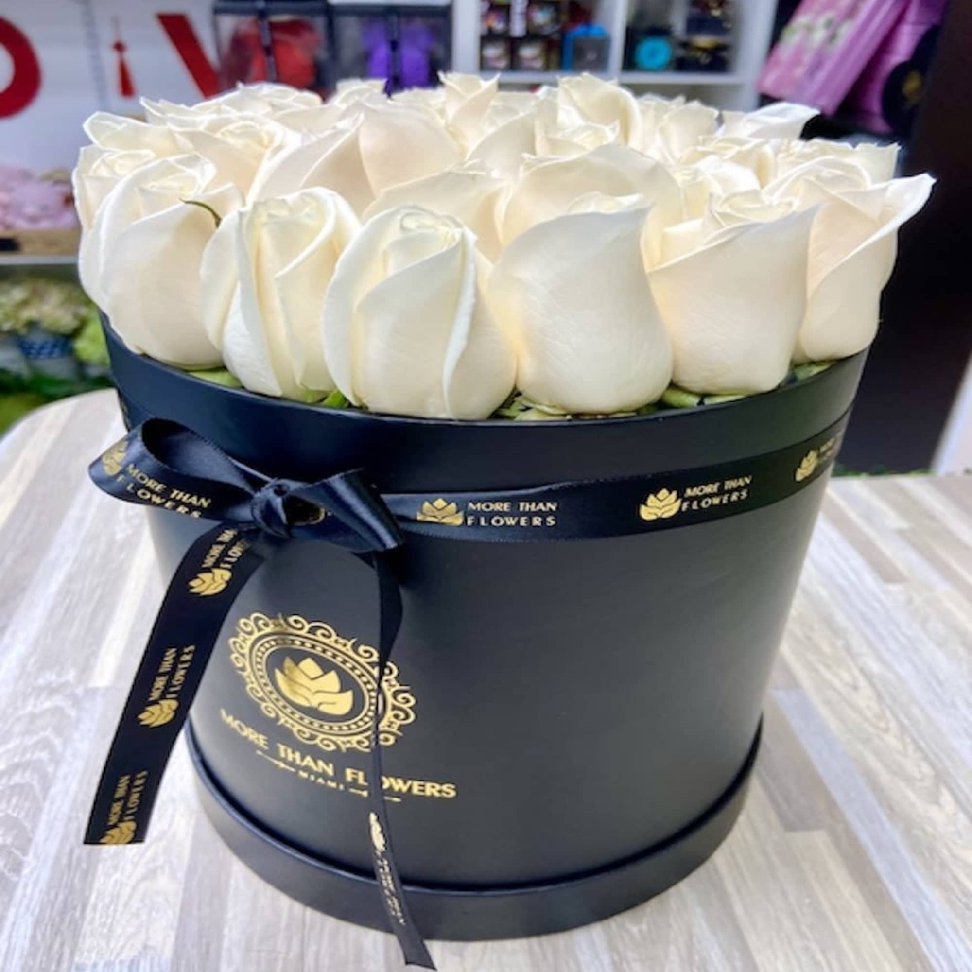 Round black hat box filled with tightly packed ivory roses and tied with a black ribbon