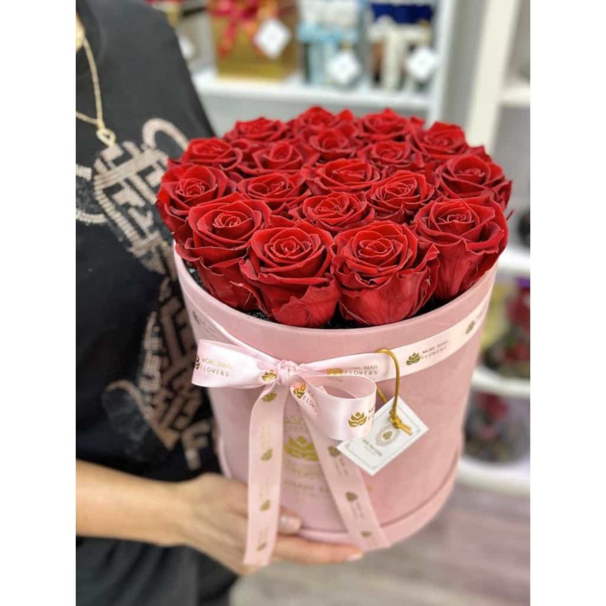 Round pink hatbox filled with tightly packed red roses and tied with a pink ribbon.
