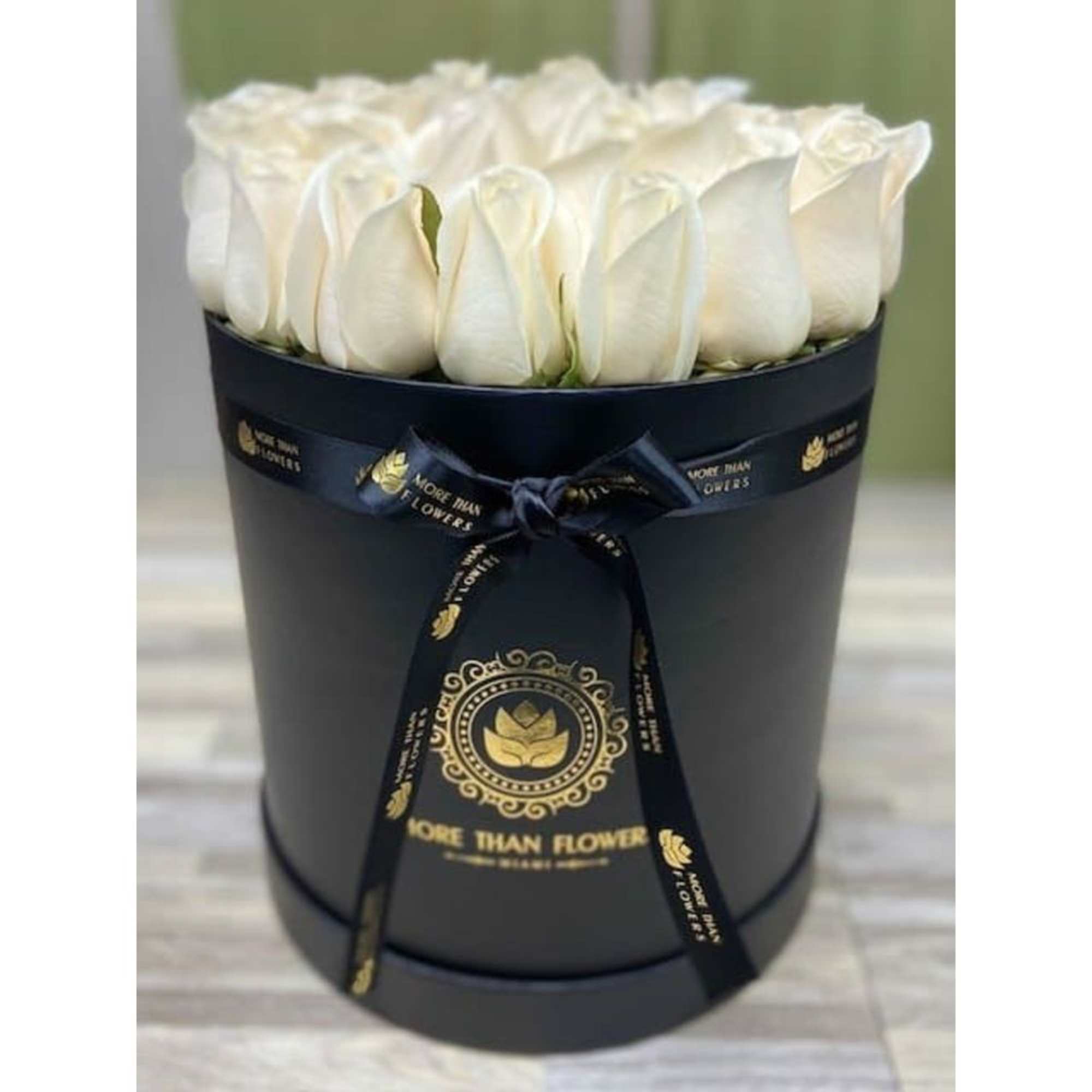 White roses arranged in a round black hatbox with a ribbon bow