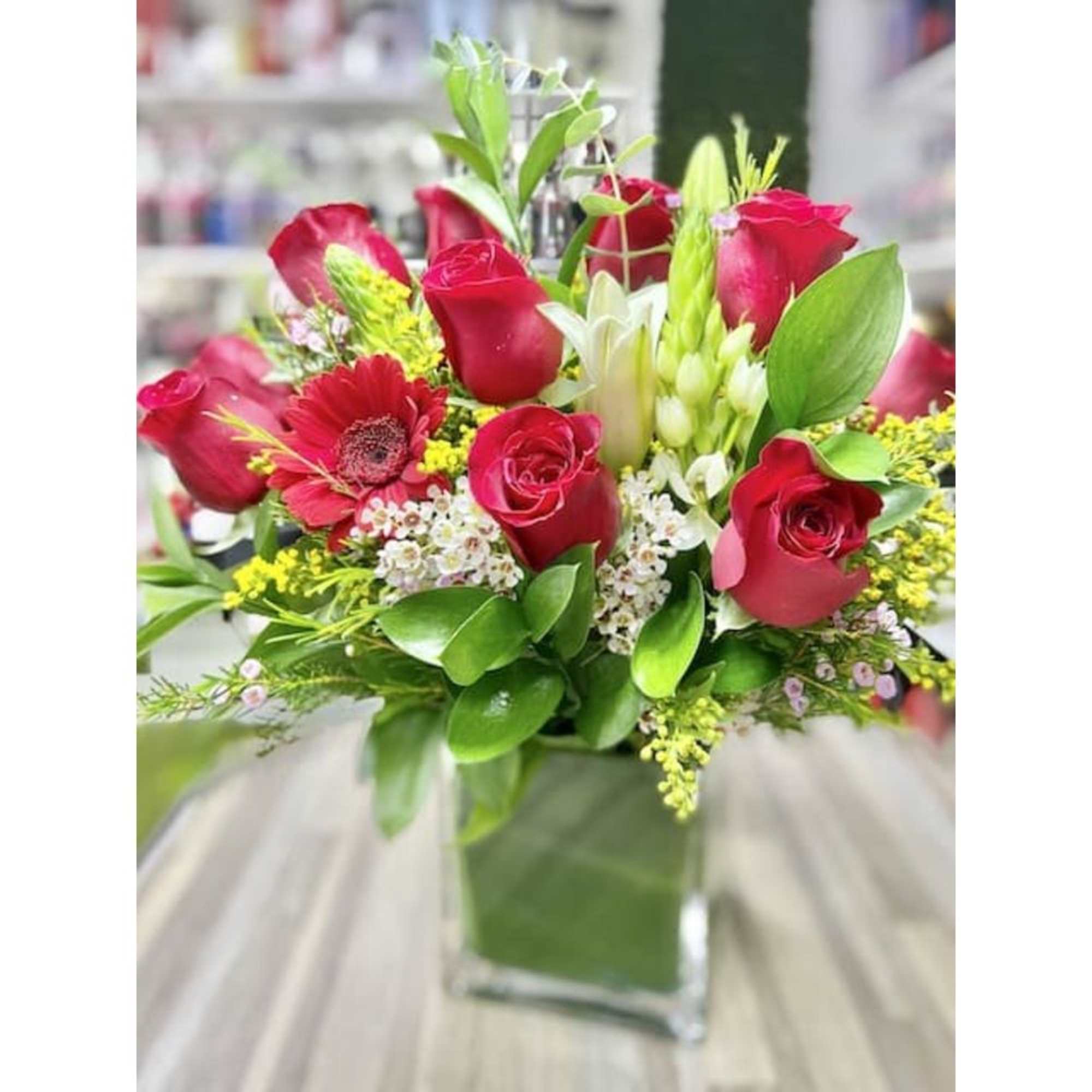 Medium arrangement of red roses and mixed flowers in a square glass vase.