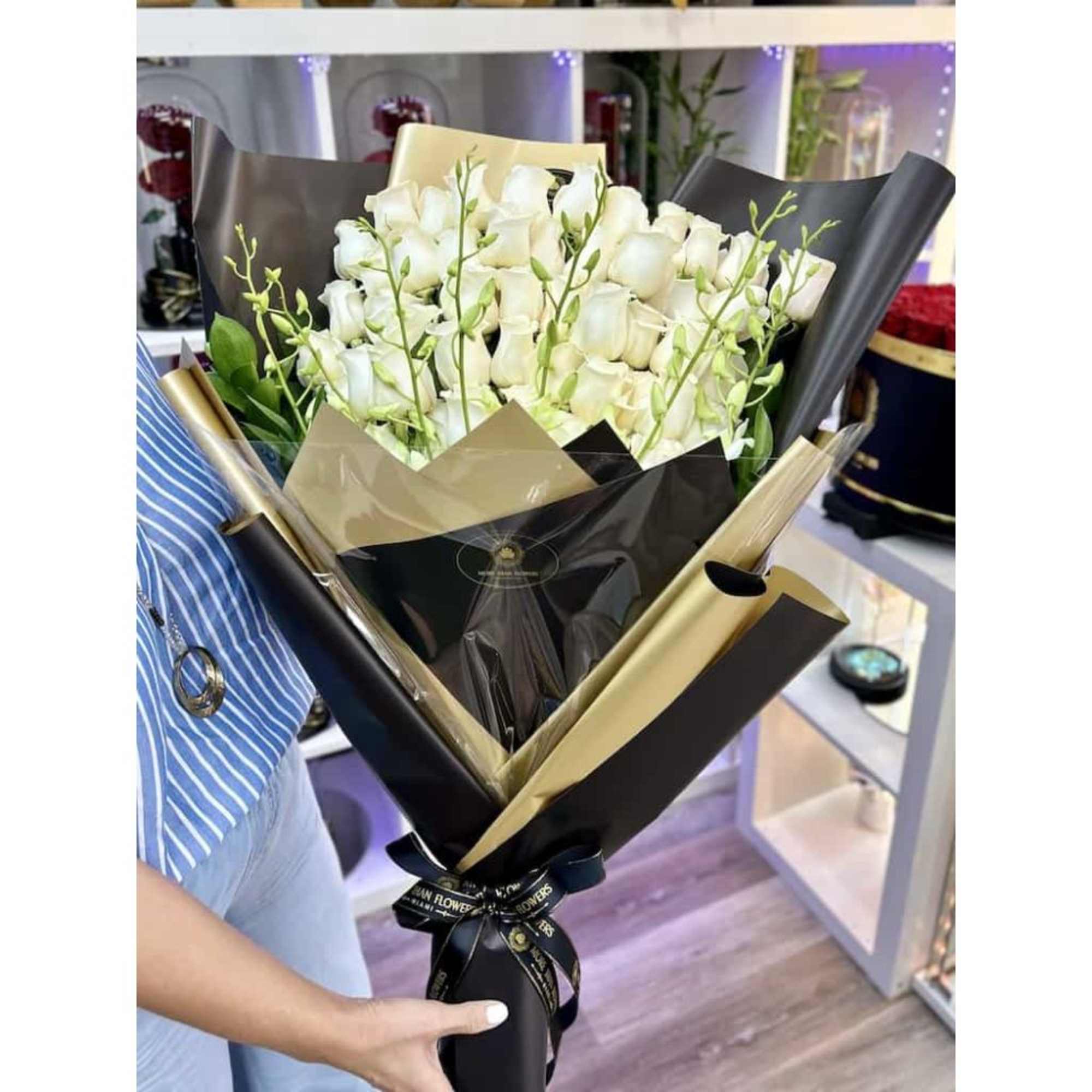 Large bouquet of white roses wrapped in black and gold paper and tied with a black ribbon.